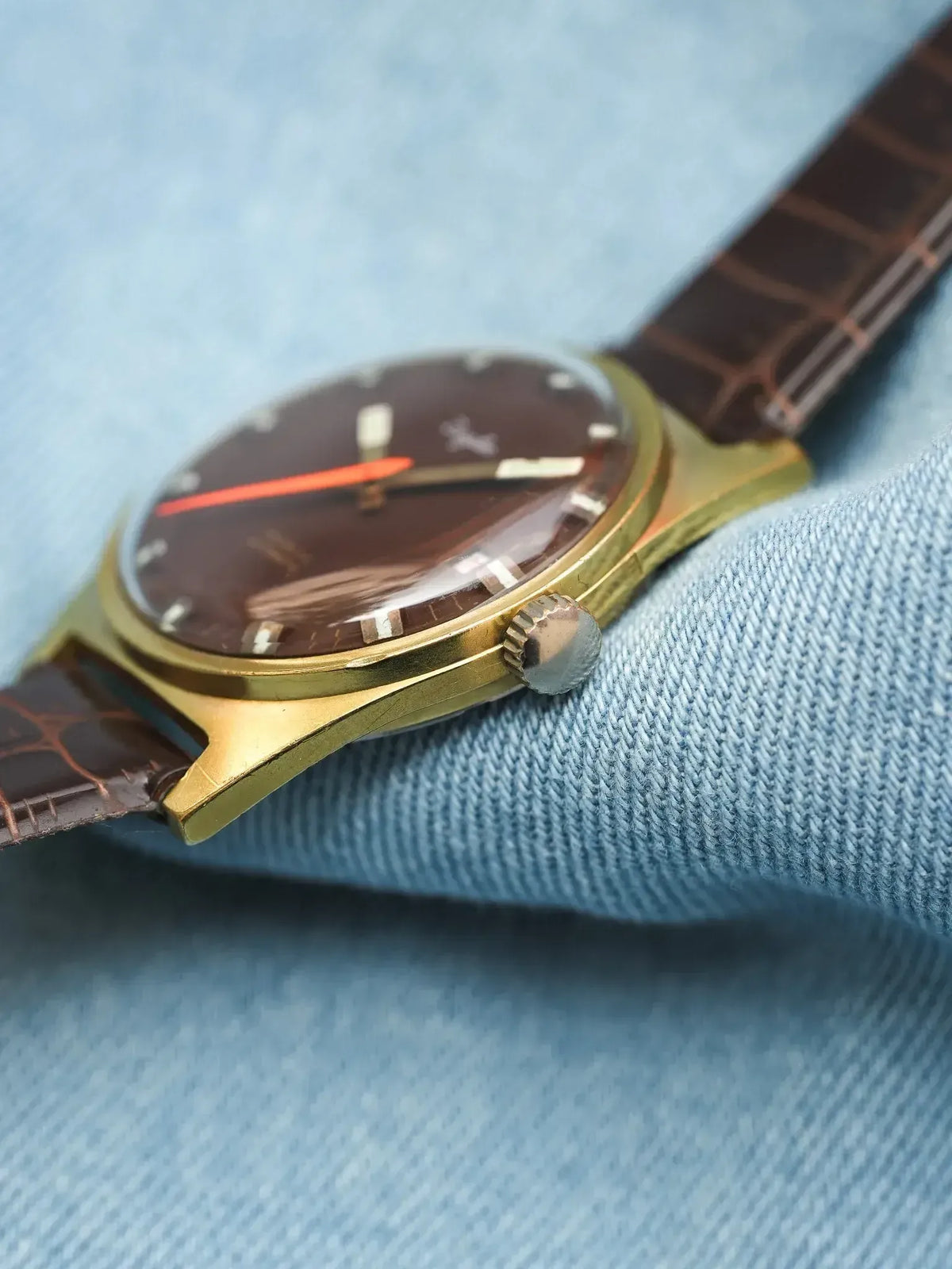 Vintage Universal Genève watch with brown dial, gold case, and brown leather strap on denim