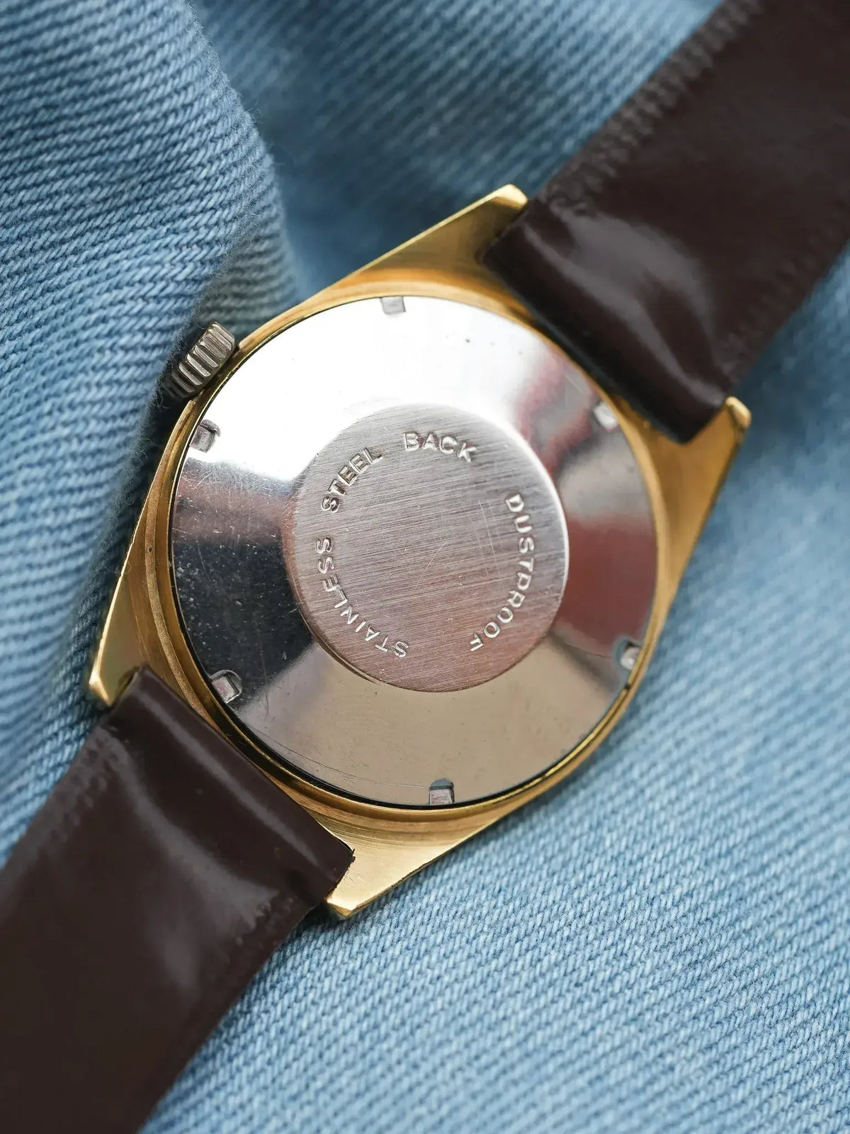 Vintage watch with gold case, brown leather strap, stainless steel back on denim