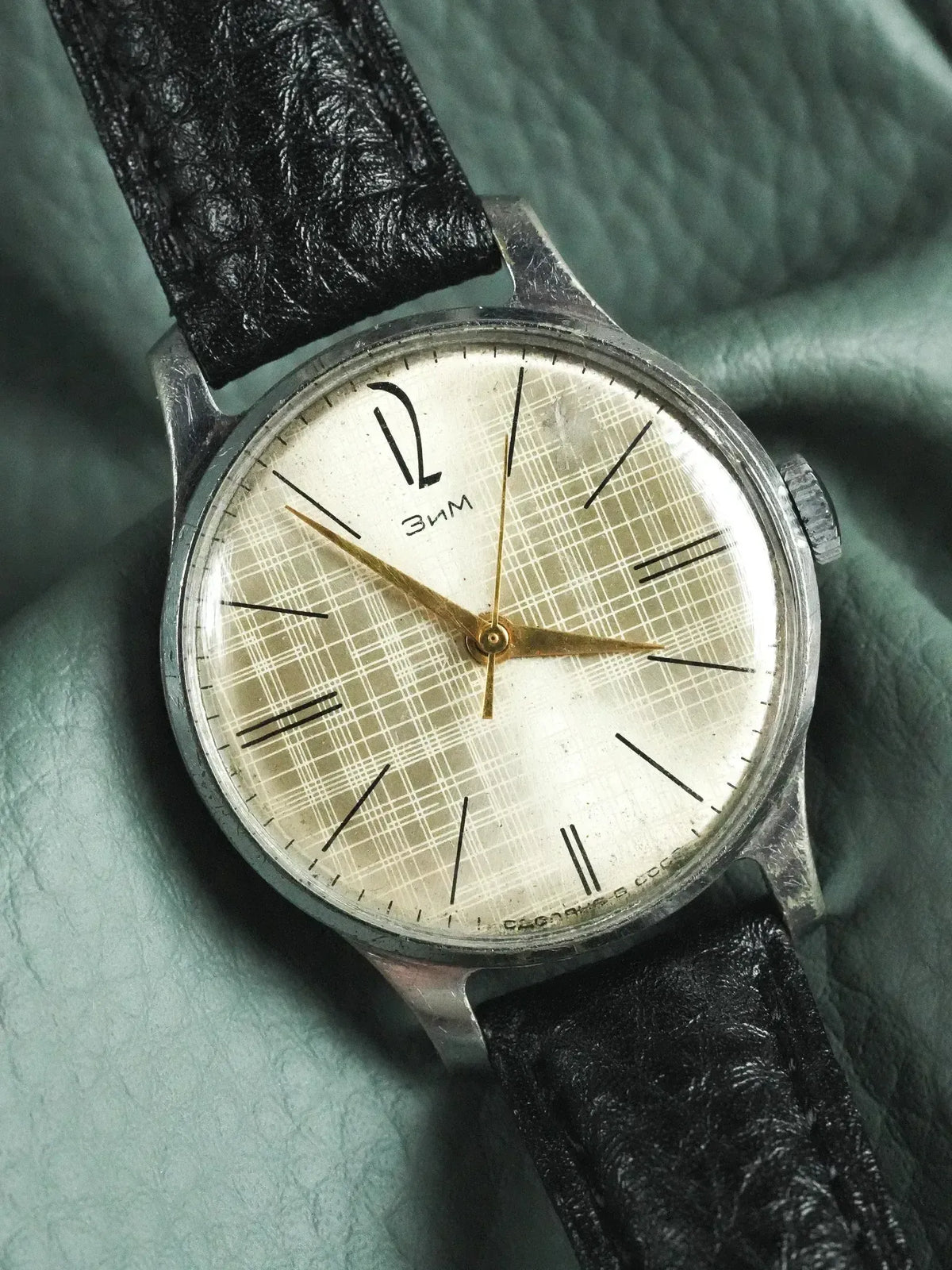 Vintage ZIM watch with silver case, cream plaid dial, black leather strap on green fabric