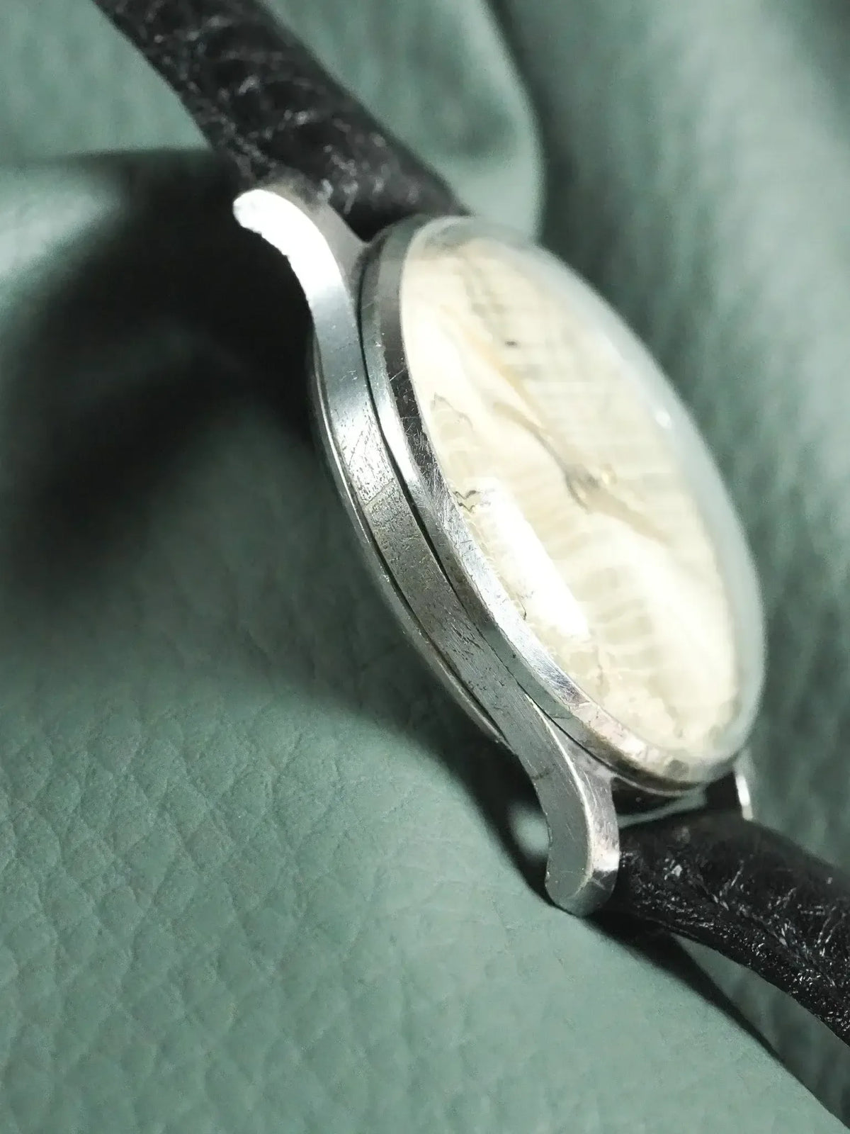 Vintage Omega watch with silver case, cream dial, black leather strap on green fabric