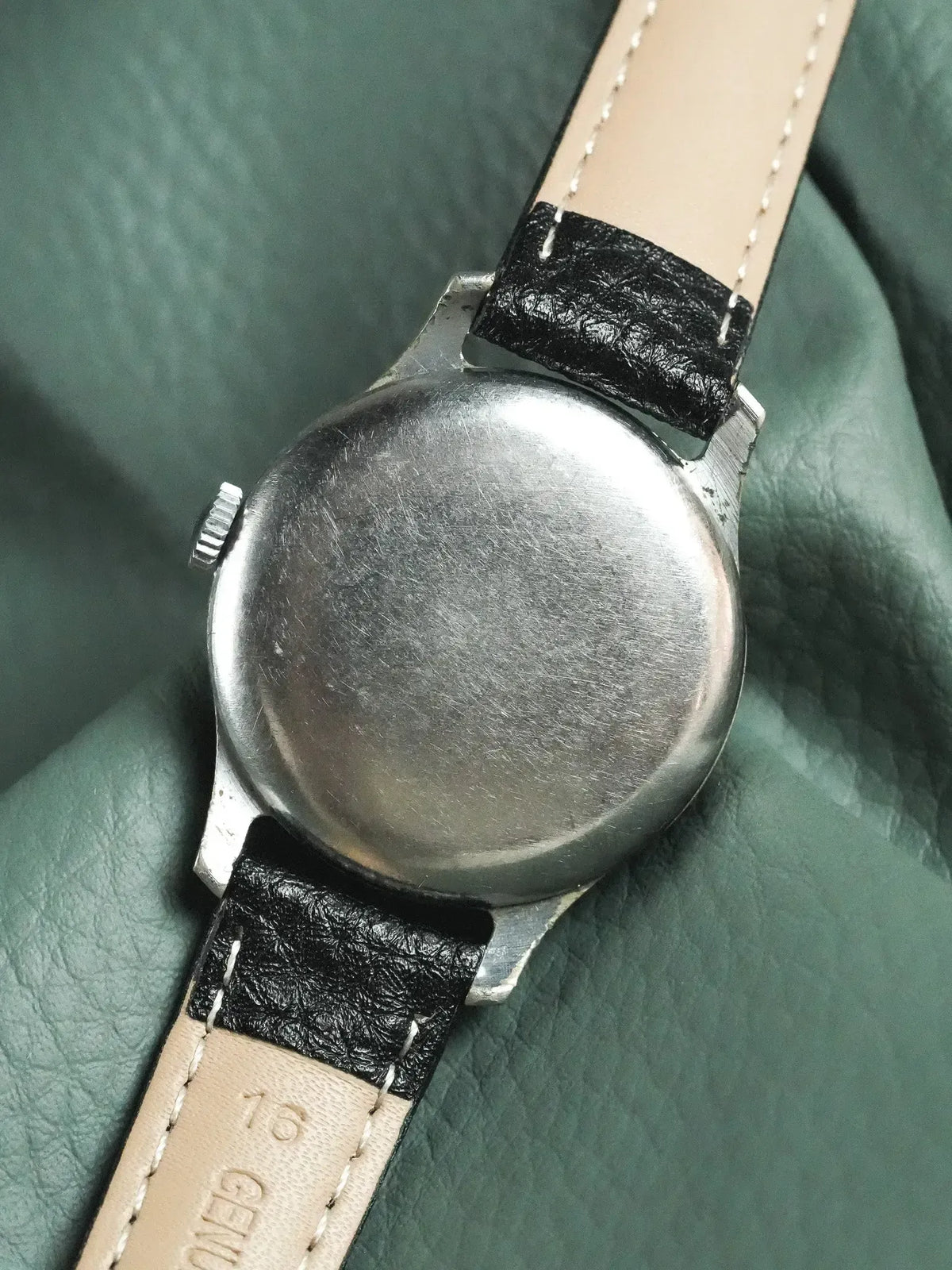 Vintage Universal Genève watch with stainless steel case and black leather strap on green background