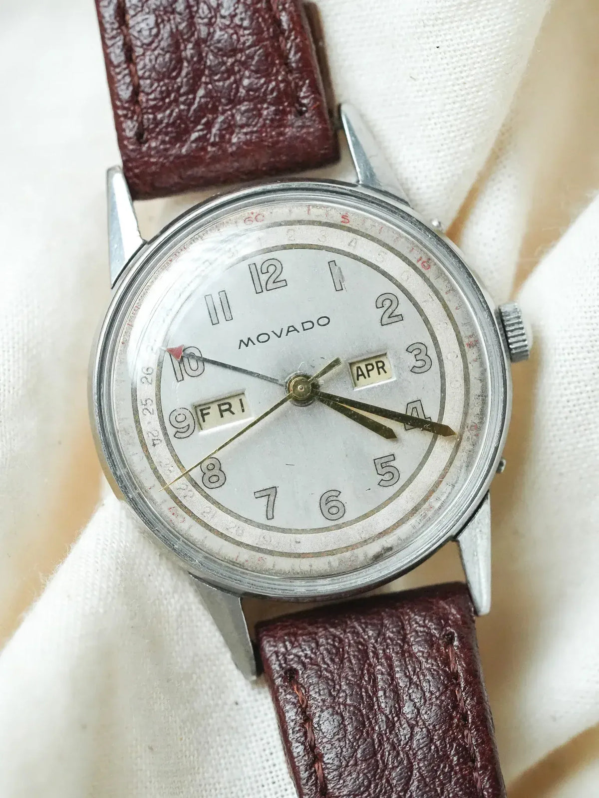 Vintage Movado watch with silver dial, day-date display, and burgundy leather strap