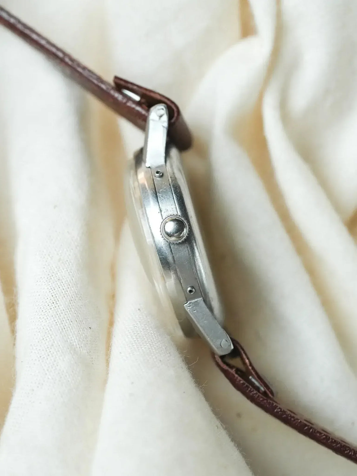 Vintage watch with silver case, brown leather strap, side view on fabric