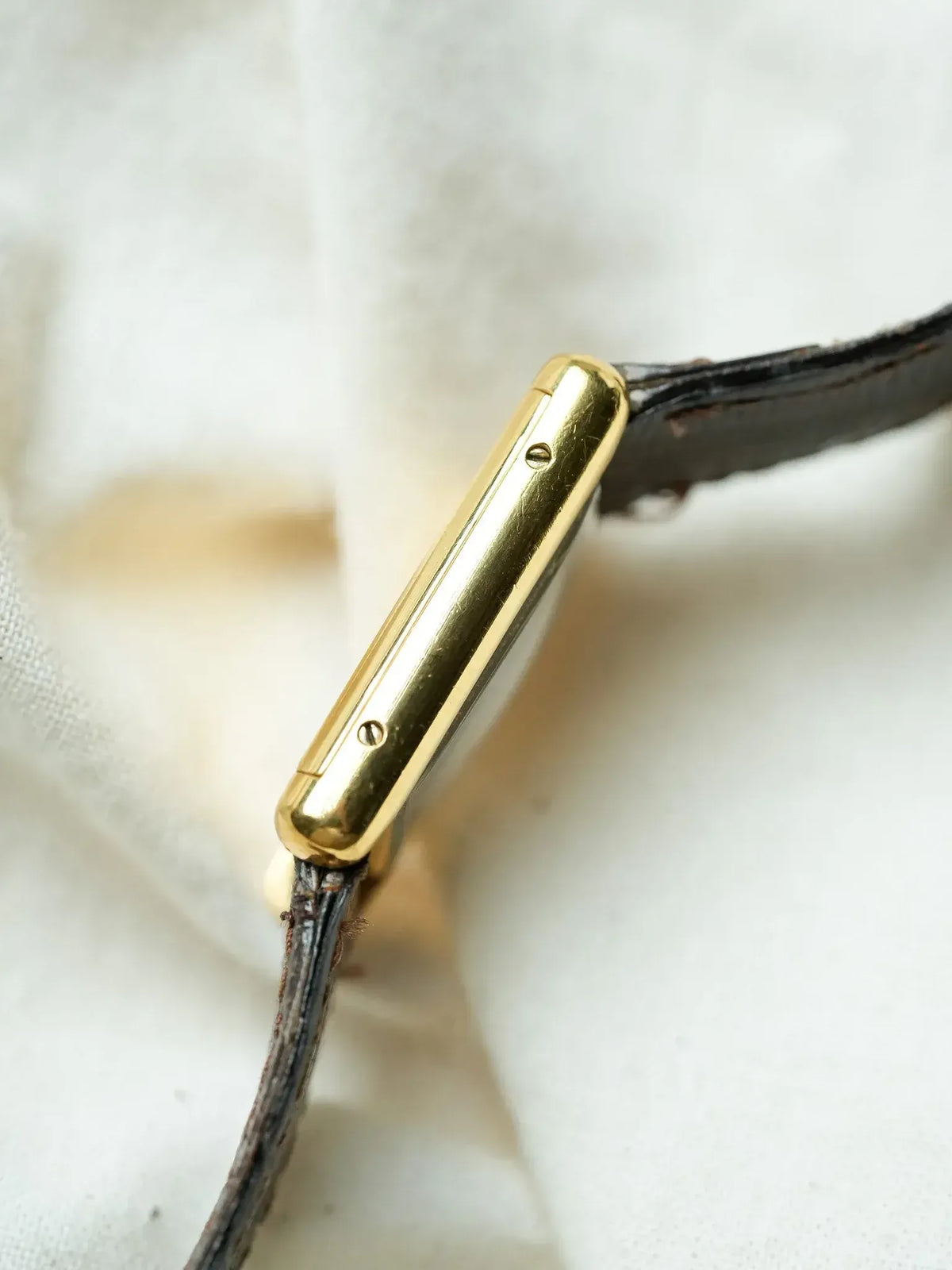 Cartier vintage watch with gold case and black leather strap on fabric