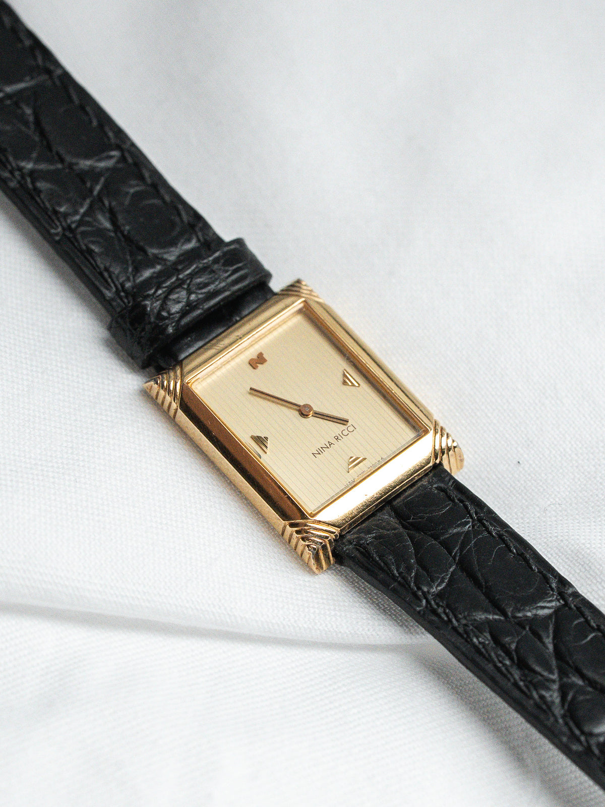 Nina Ricci vintage gold watch with black leather strap, rectangular case, cream dial