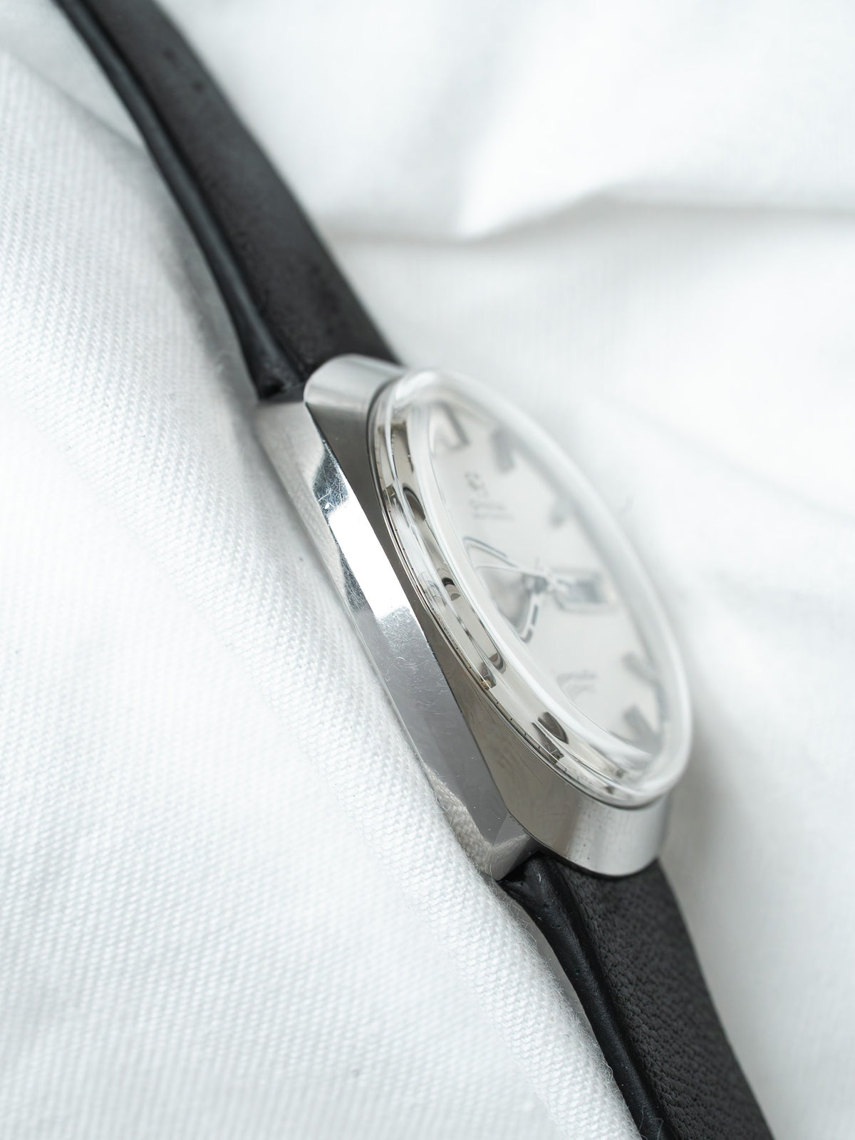 Vintage Omega watch with silver case, white dial, black leather strap on white fabric