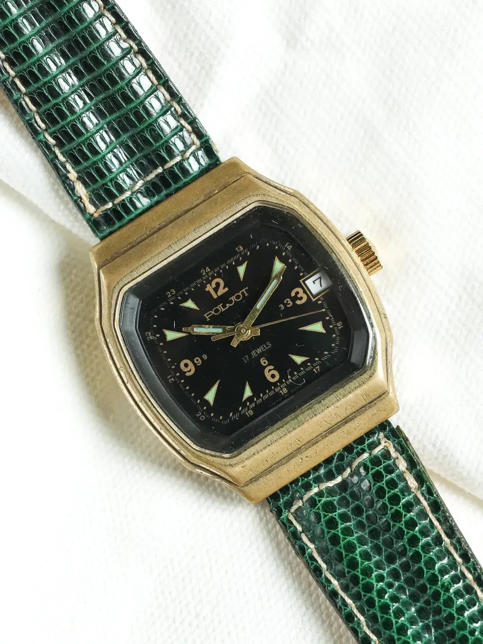 Poljot vintage watch with gold case, black dial, green lizard strap on white background