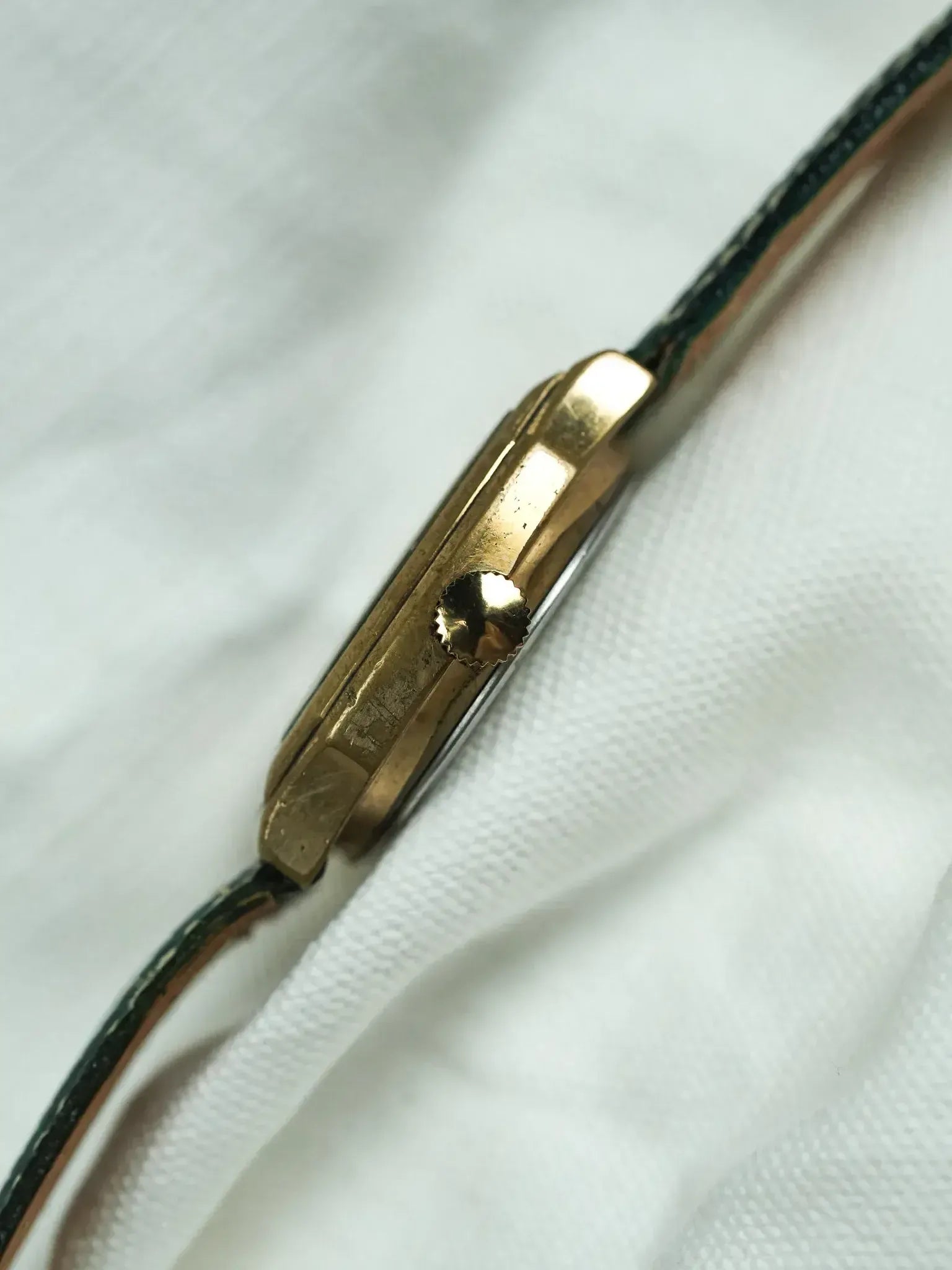 Vintage Cartier Tank watch with gold case and dark green leather strap on white fabric