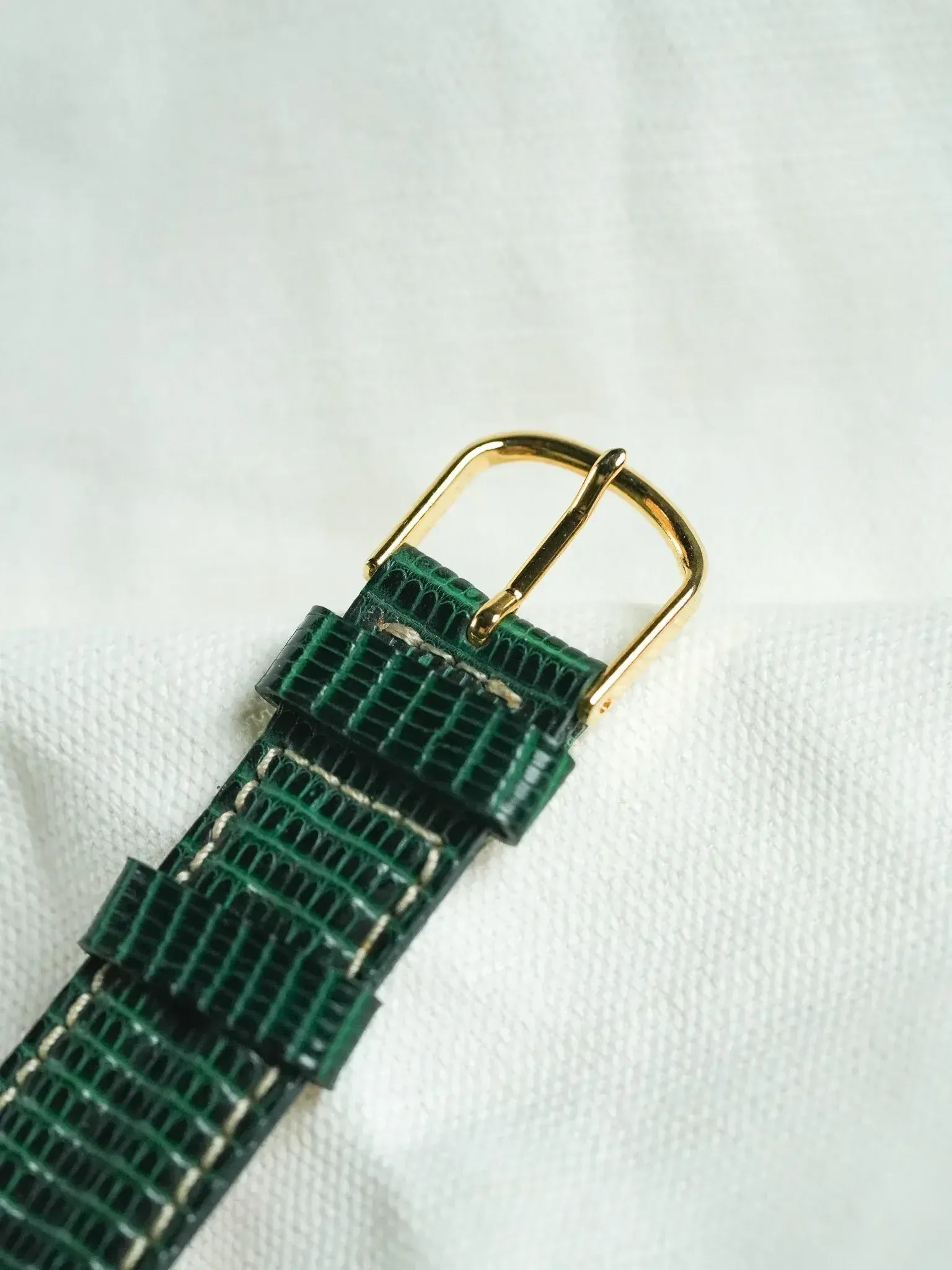 Green textured leather watch strap with gold buckle on white background