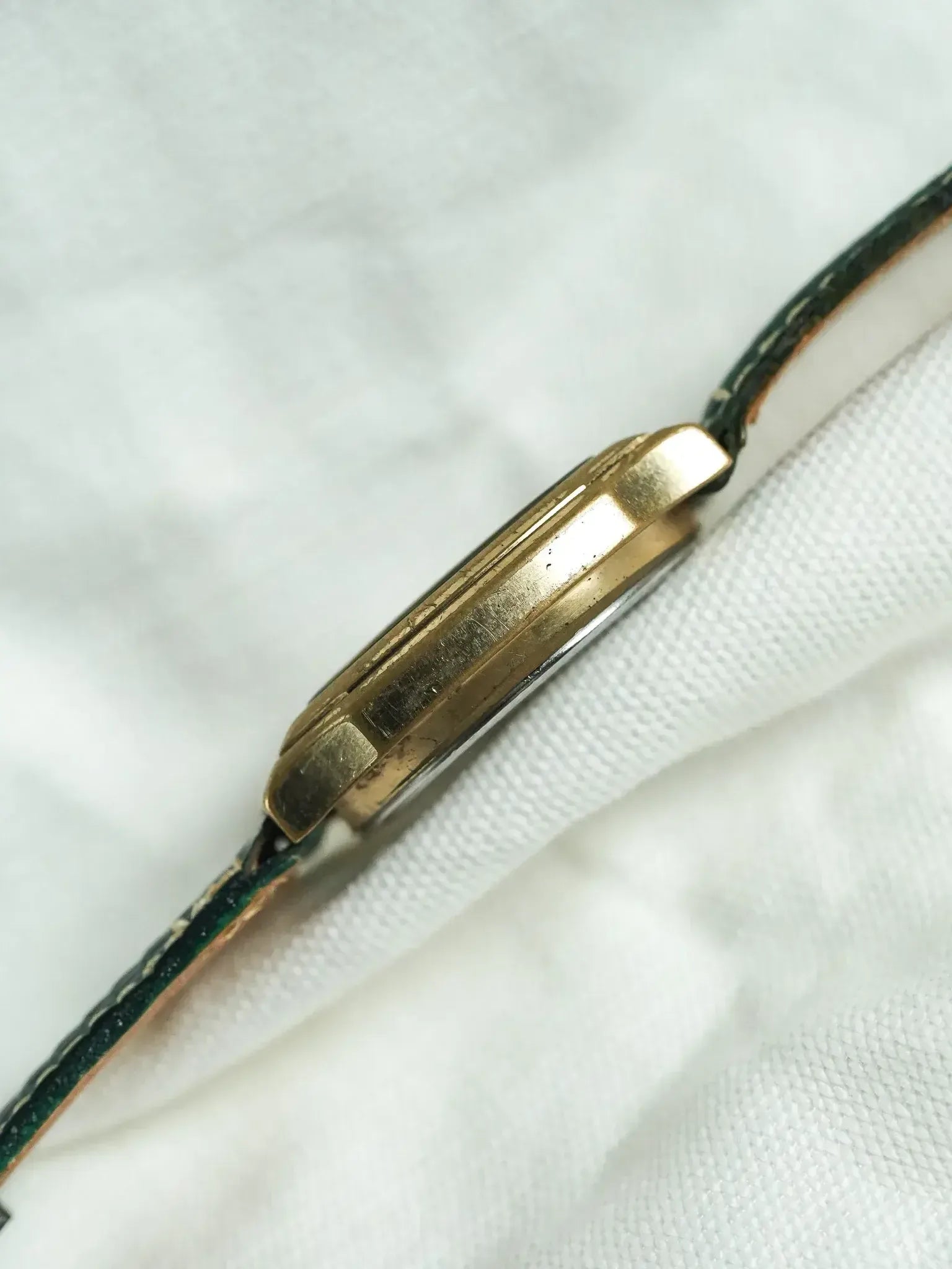Vintage Cartier Tank watch with gold case and green leather strap on white fabric