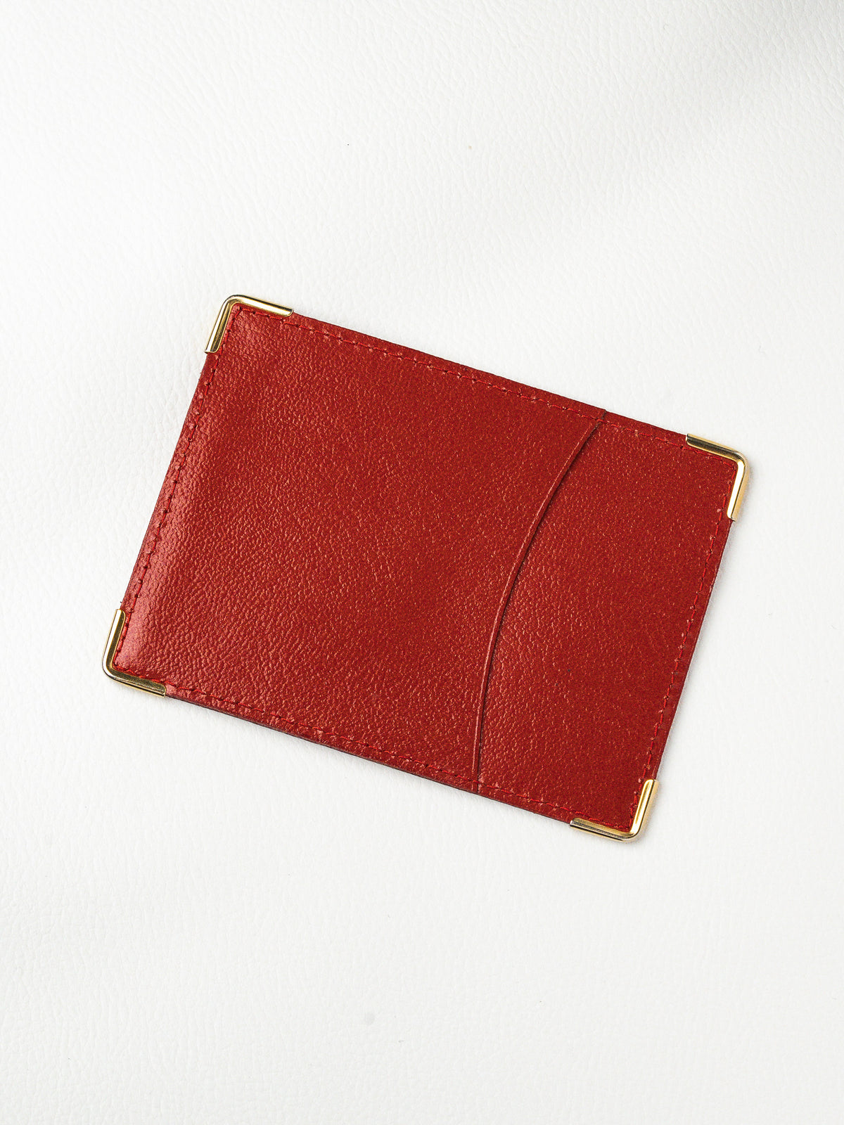 Red leather cardholder with gold corner accents, minimalist design on white background