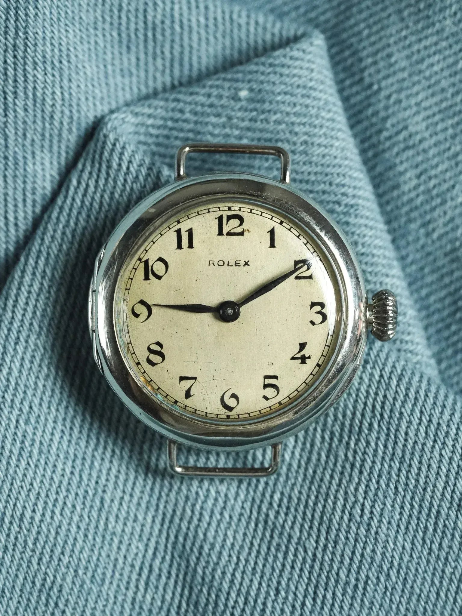Vintage Rolex wristwatch with cream dial, black numerals, and silver case on denim