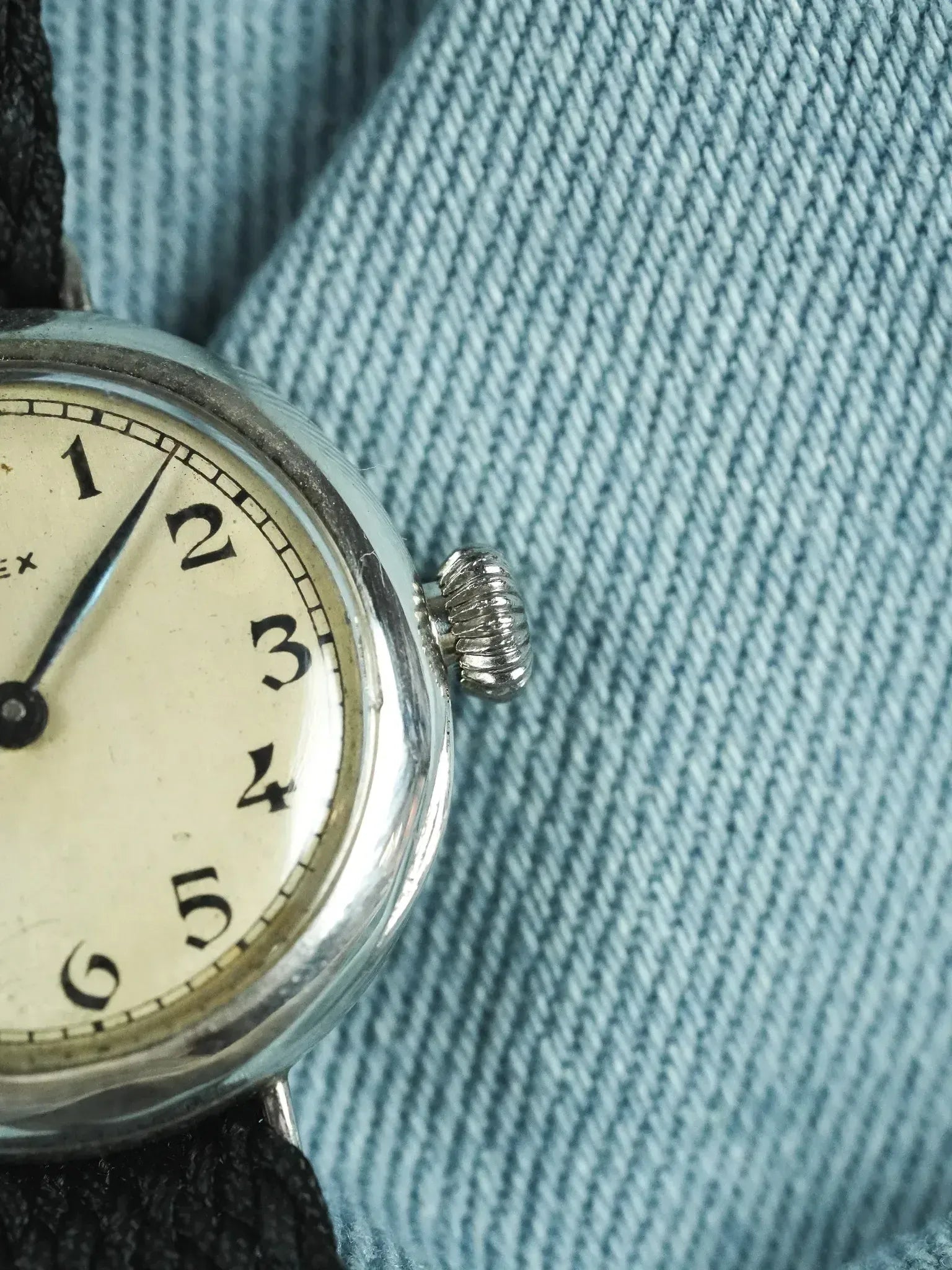 Vintage Rolex watch with cream dial, black numerals, and textured crown on denim