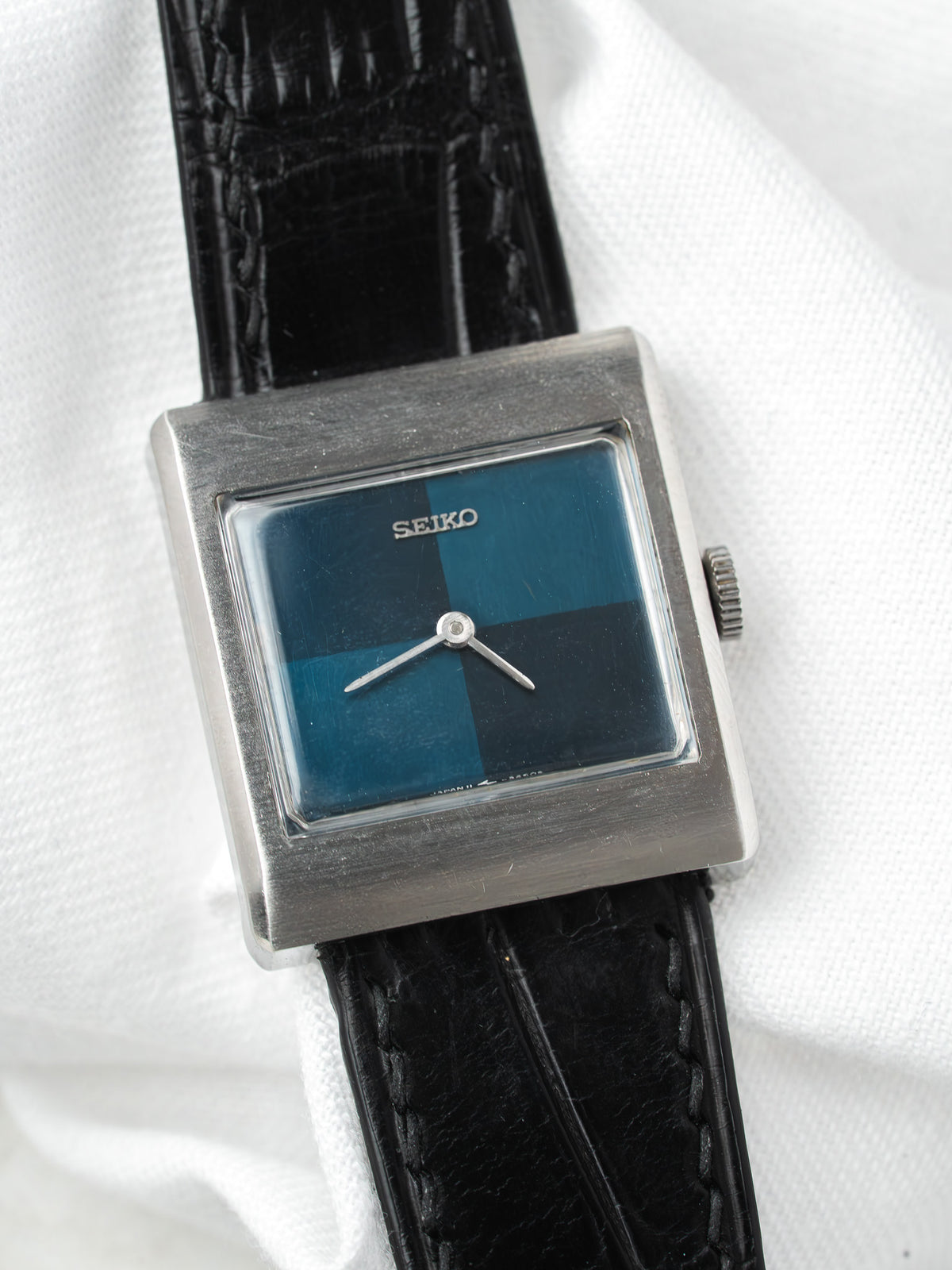 Seiko vintage square watch with blue-black dial, steel case, black leather strap on white fabric