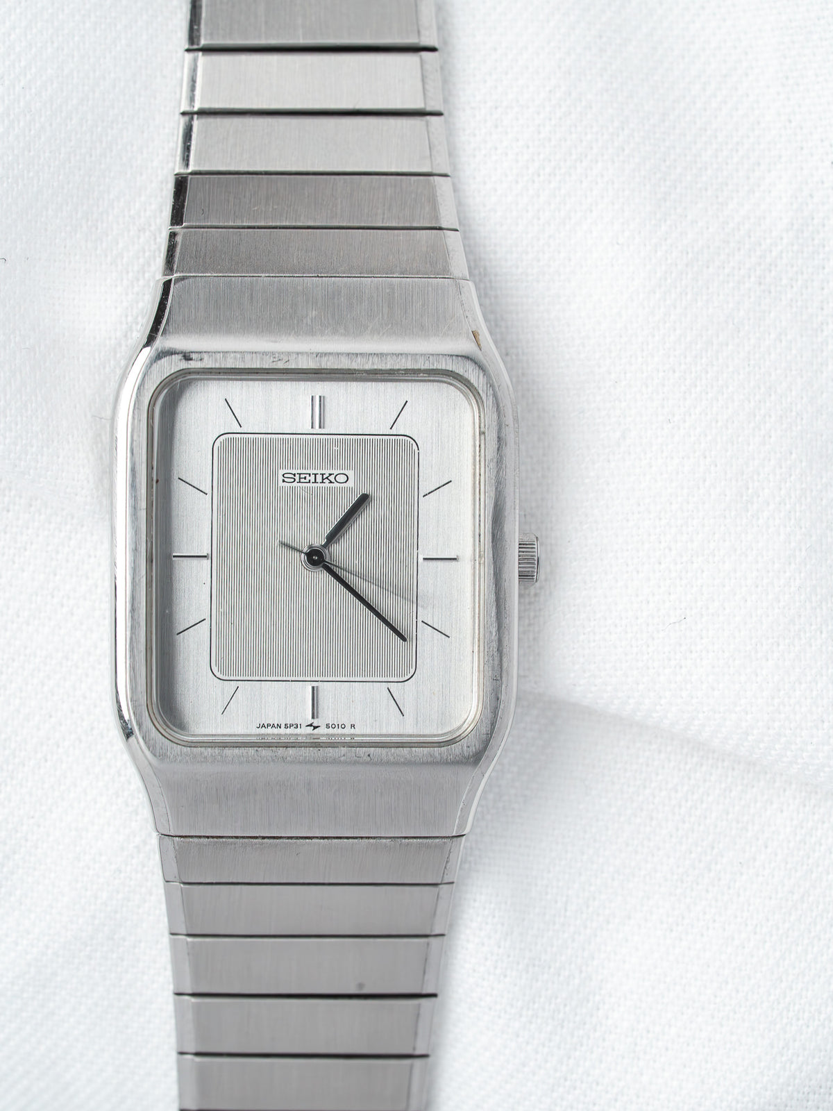 Vintage Seiko square watch with silver dial and matching metal bracelet on white background