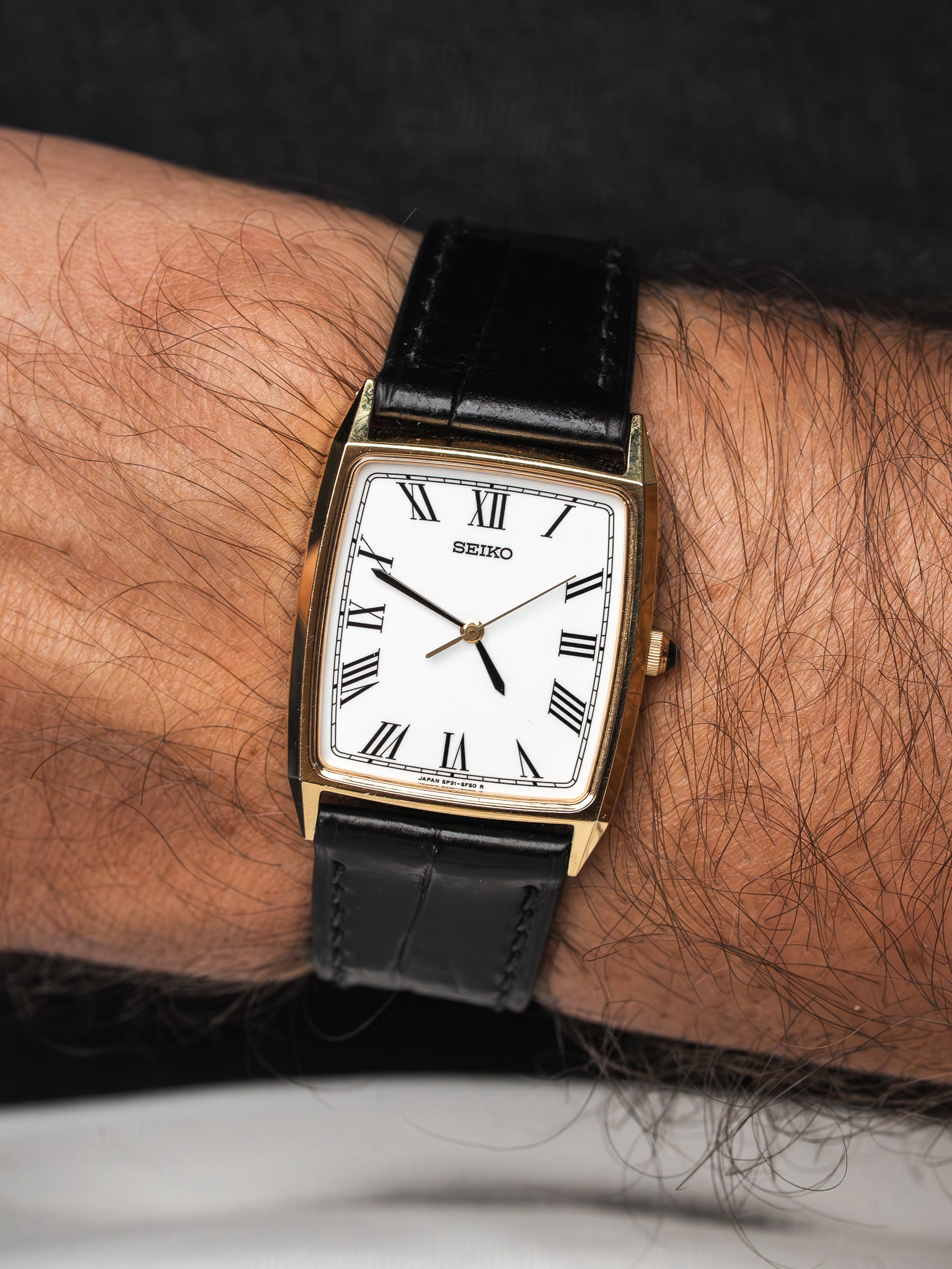 Seiko vintage watch with gold case, white dial, Roman numerals, black leather strap on wrist