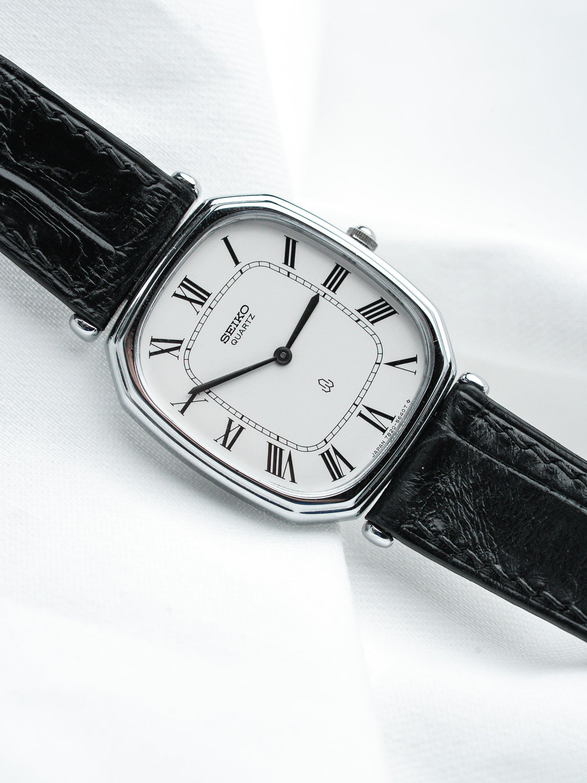 Seiko Quartz vintage watch with white dial, Roman numerals, black leather strap on white background