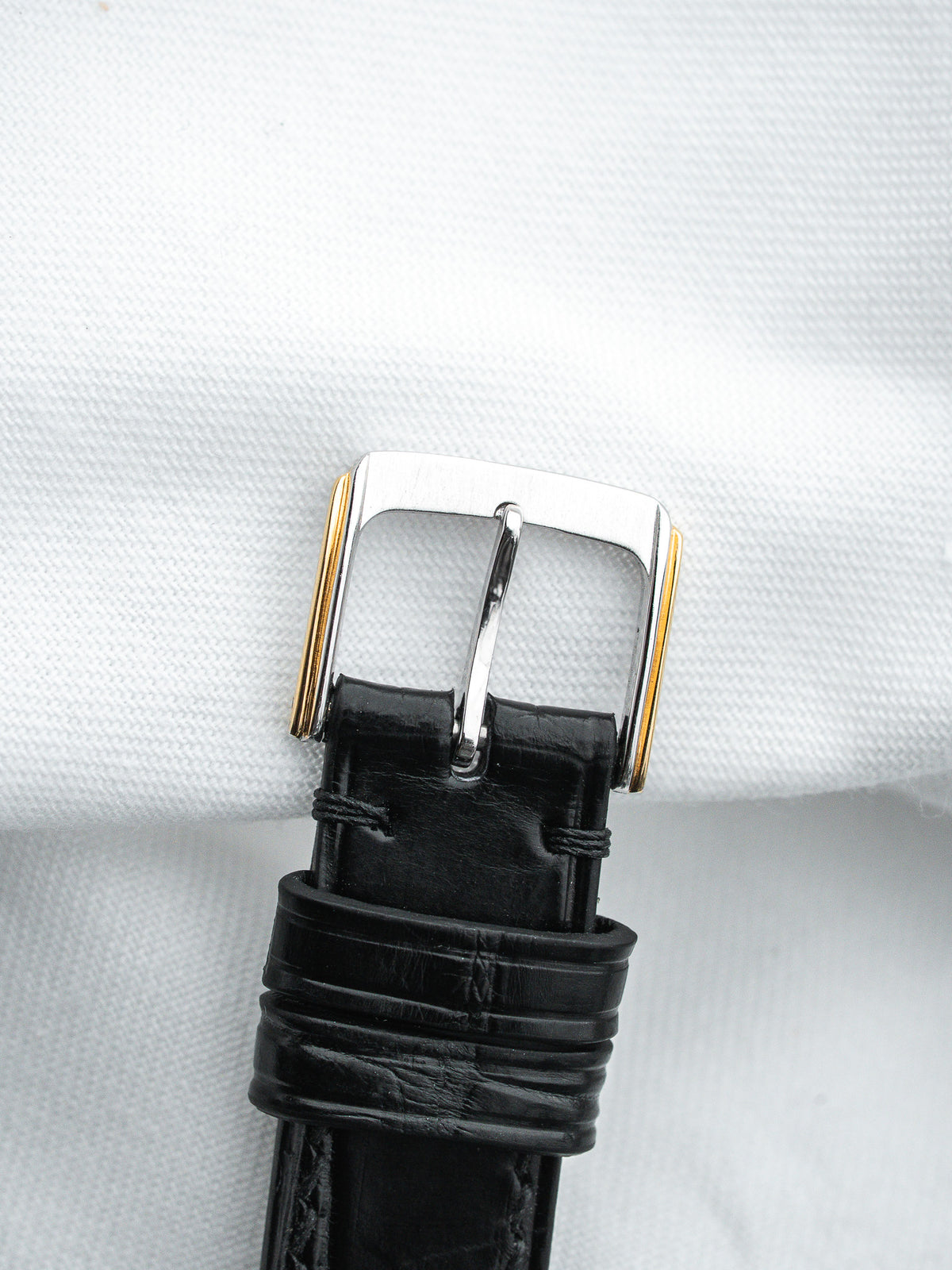 Black leather watch strap with two-tone buckle on white background