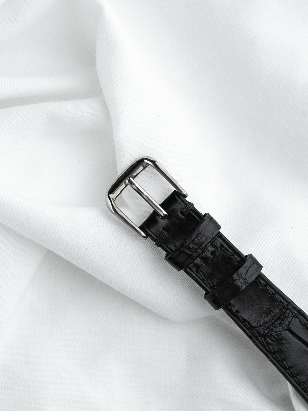 Bracelet de montre en cuir noir embossé avec boucle argentée sur fond blanc