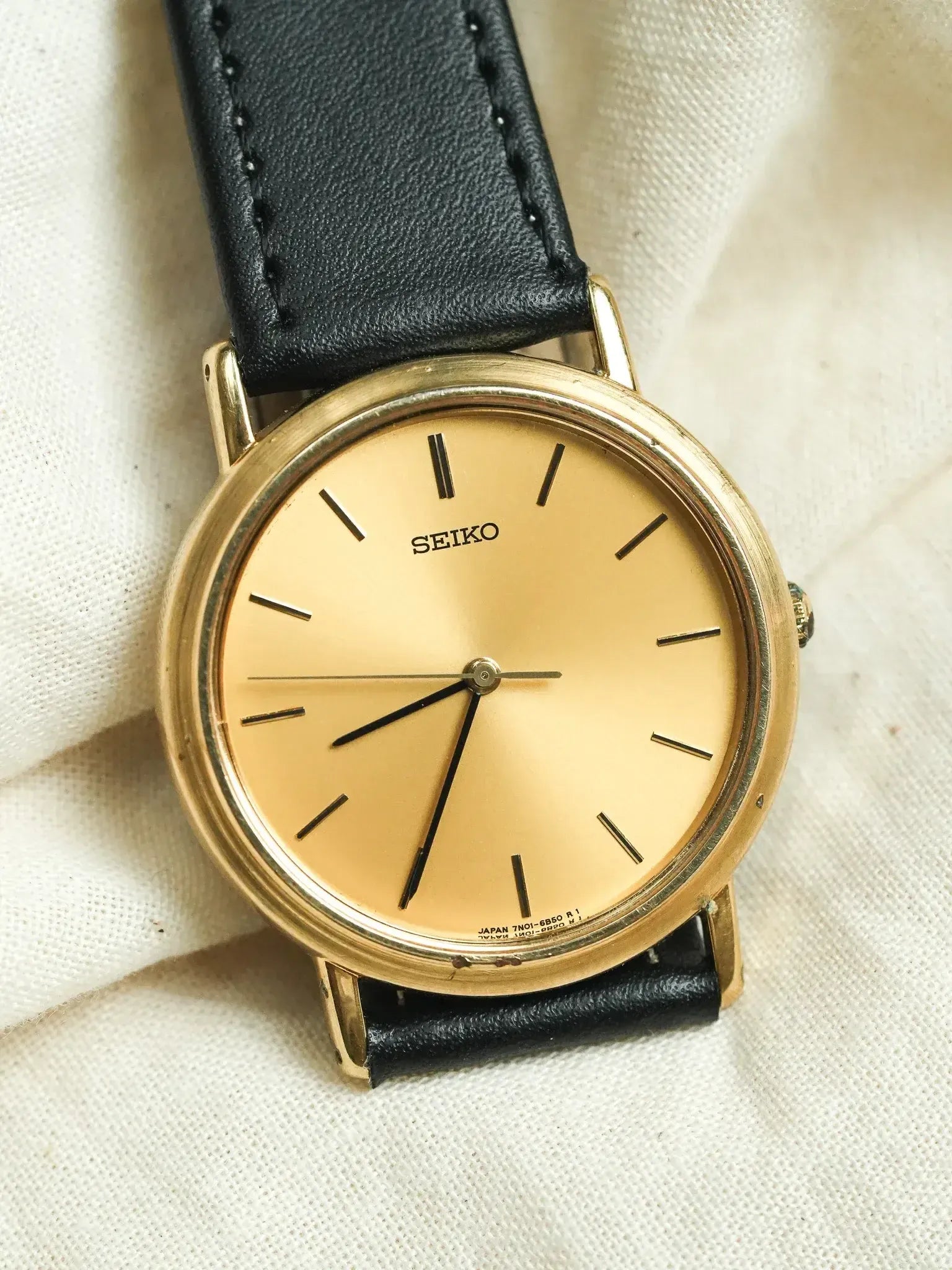 Vintage Seiko watch with gold case, cream dial, black leather strap on fabric