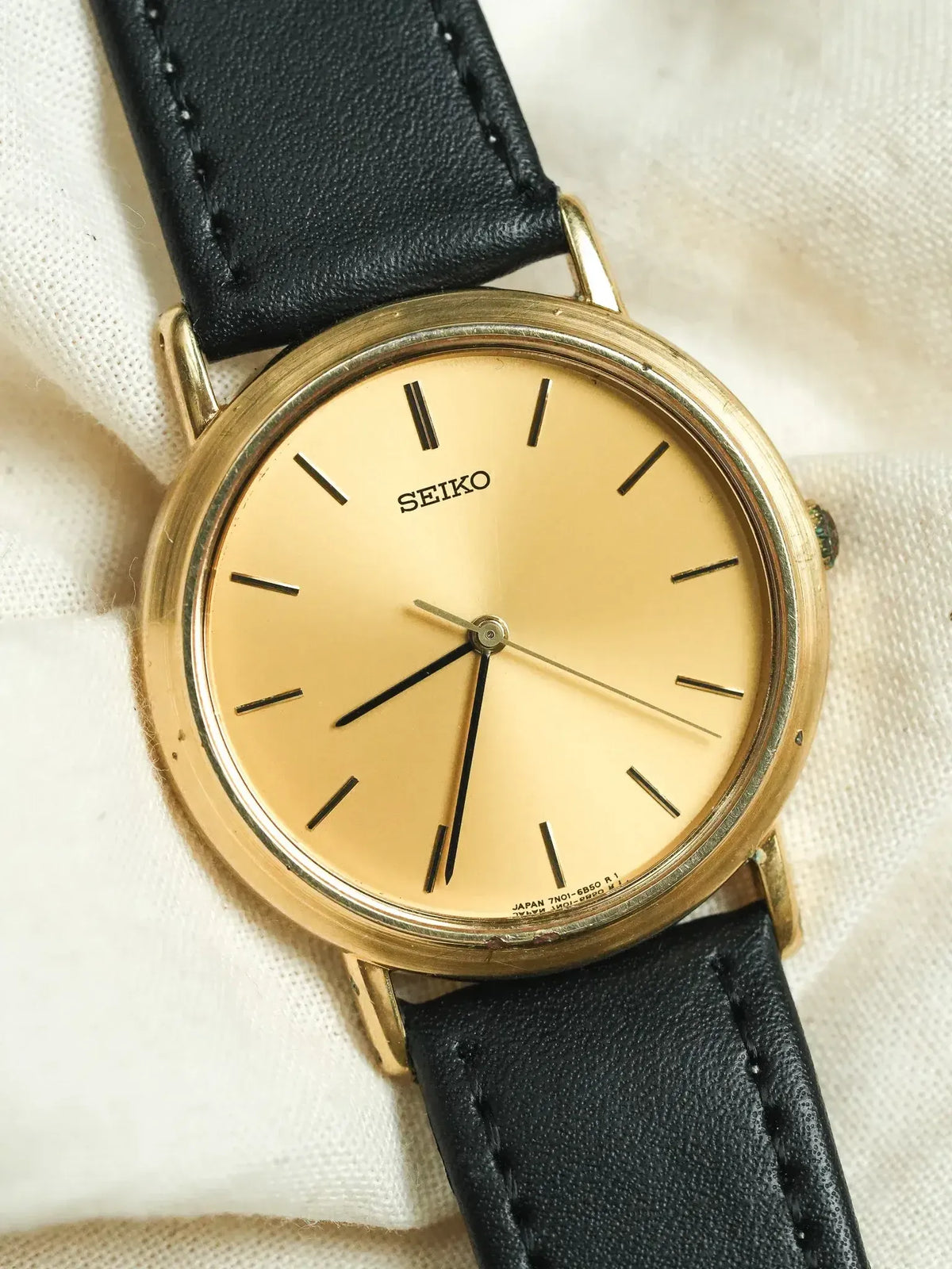 Seiko vintage watch with gold case, champagne dial, black leather strap on fabric