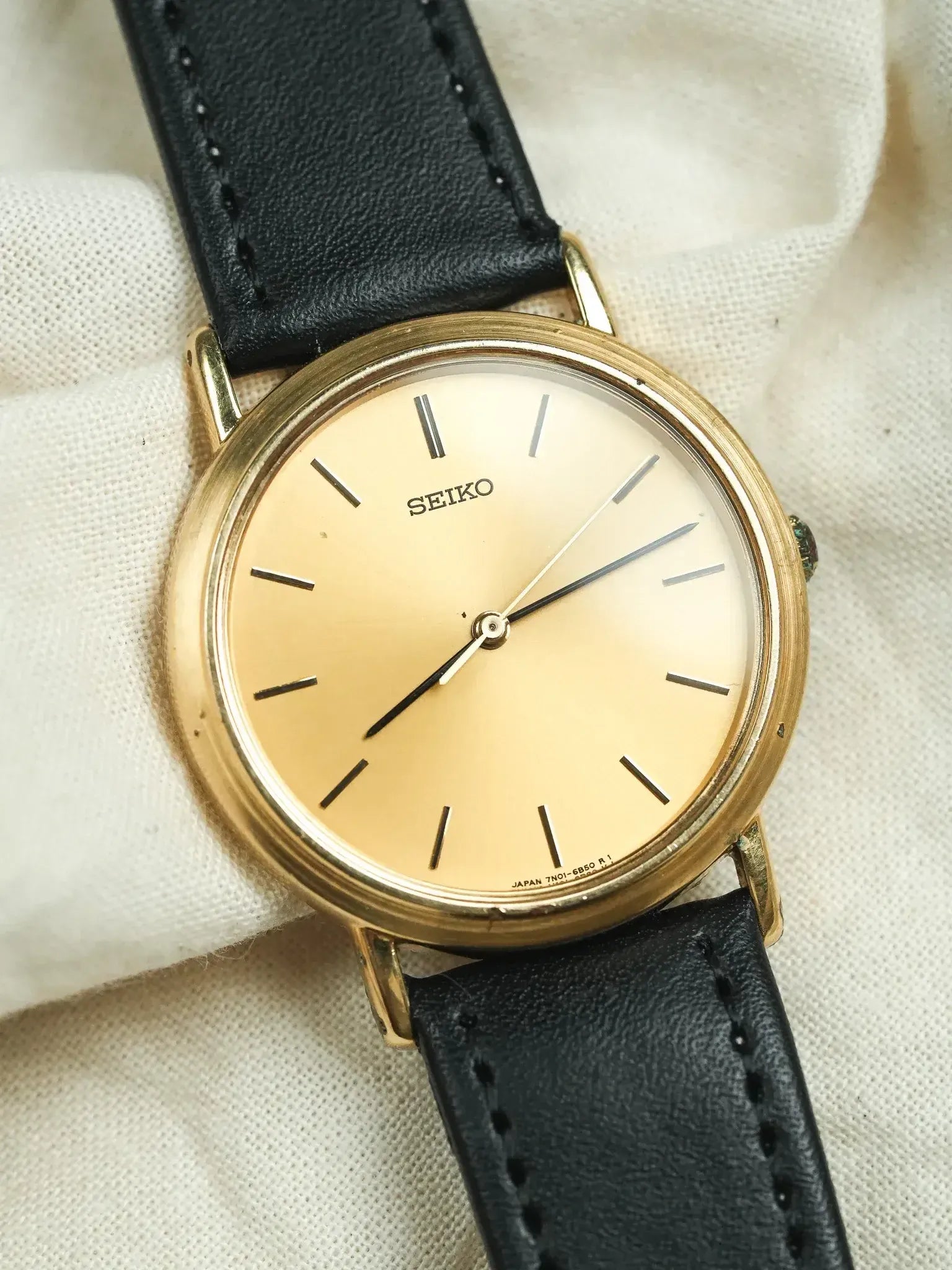 Seiko vintage watch with gold case, cream dial, black leather strap on fabric