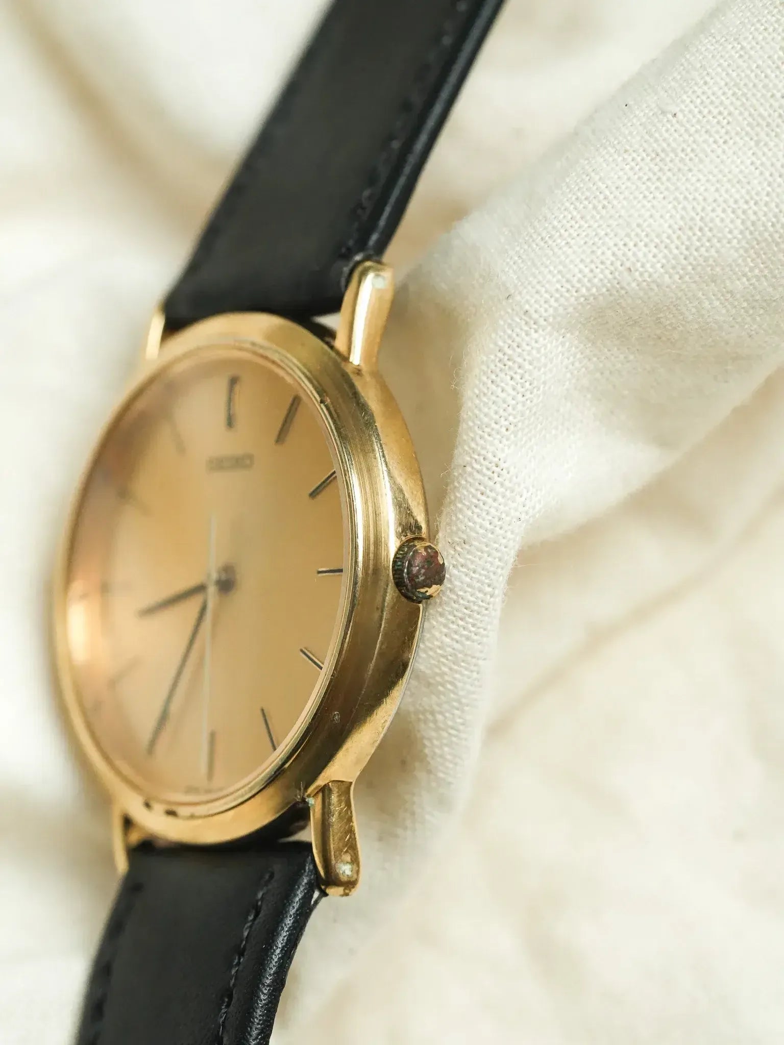 Vintage Seiko watch with gold case, cream dial, black leather strap on fabric