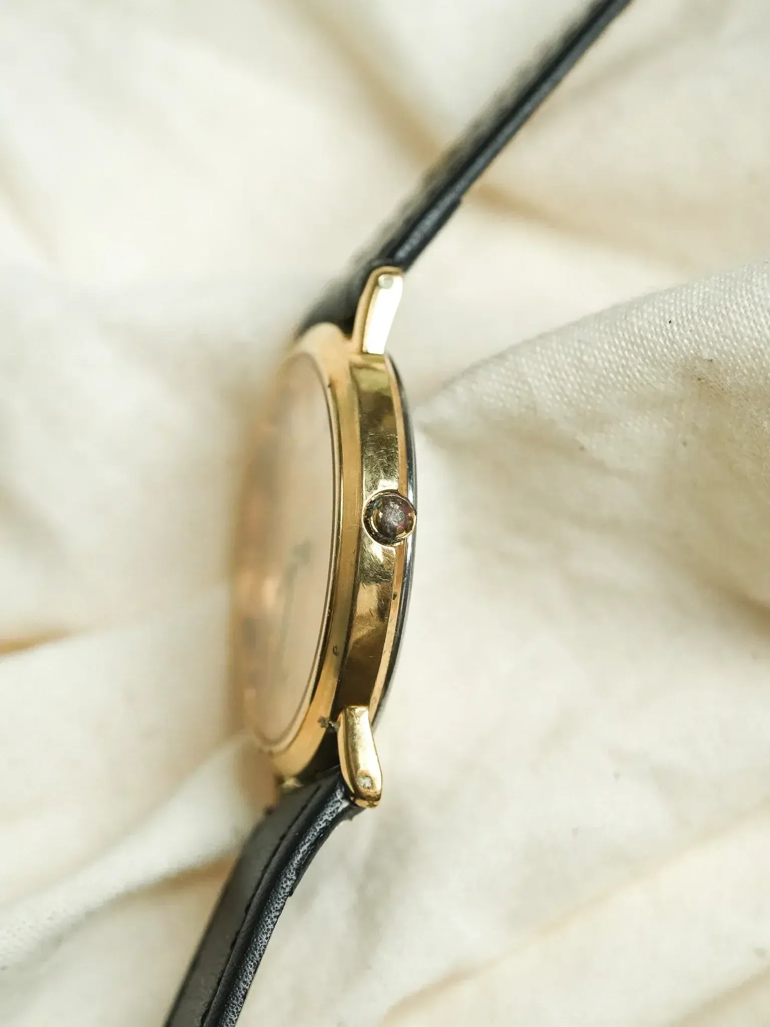 Vintage Cartier watch with gold case and black leather strap on fabric