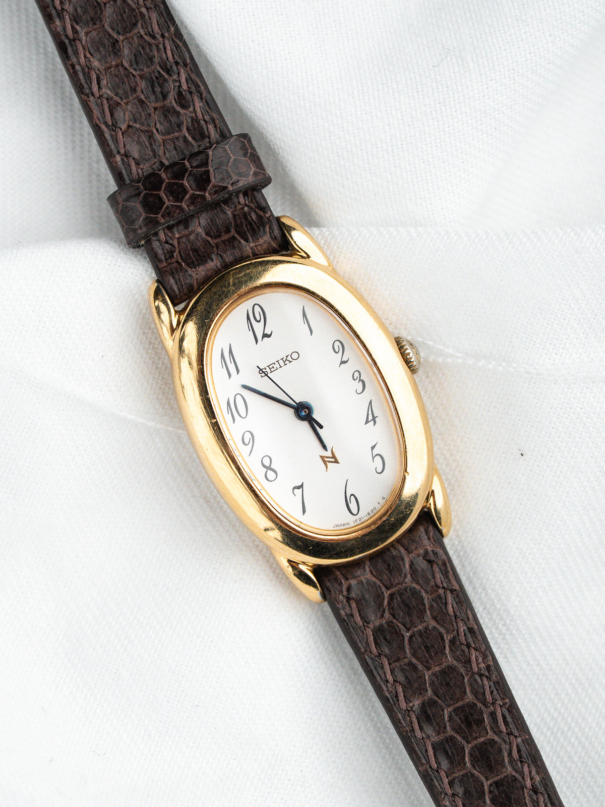 Seiko vintage watch with gold case, white dial, and brown textured strap