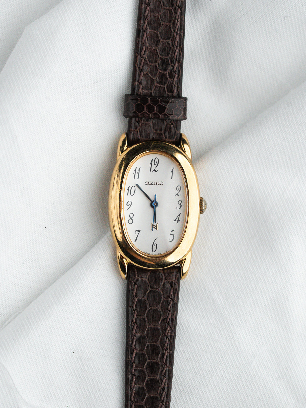 Seiko vintage watch with gold case, white dial, and brown textured strap