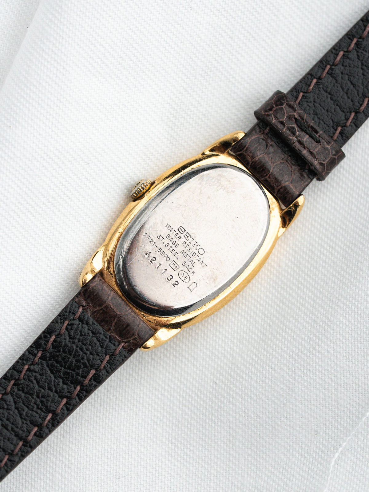 Seiko vintage watch with gold case, brown leather strap, and engraved case back on white fabric