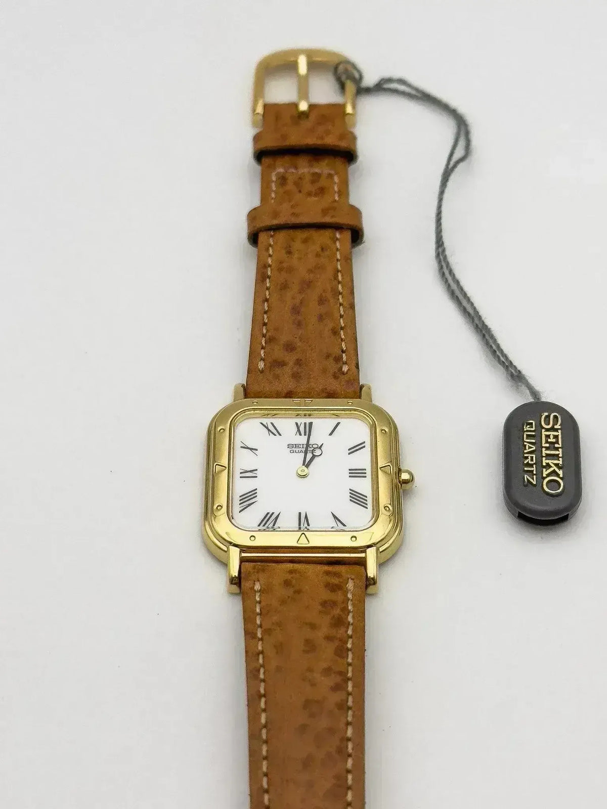 Seiko quartz watch with gold case, white dial, Roman numerals, and brown leather strap