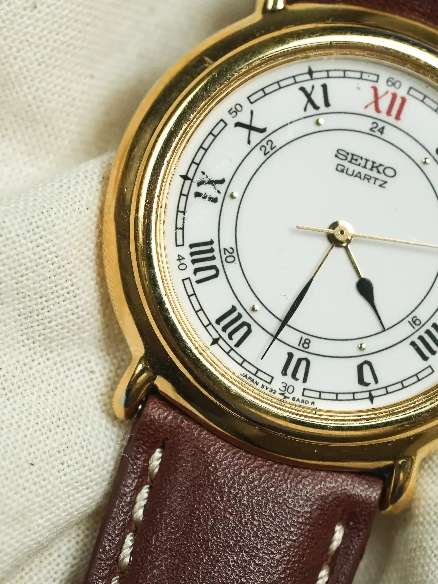 Seiko Quartz vintage watch with gold case, white dial, Roman numerals, and brown leather strap