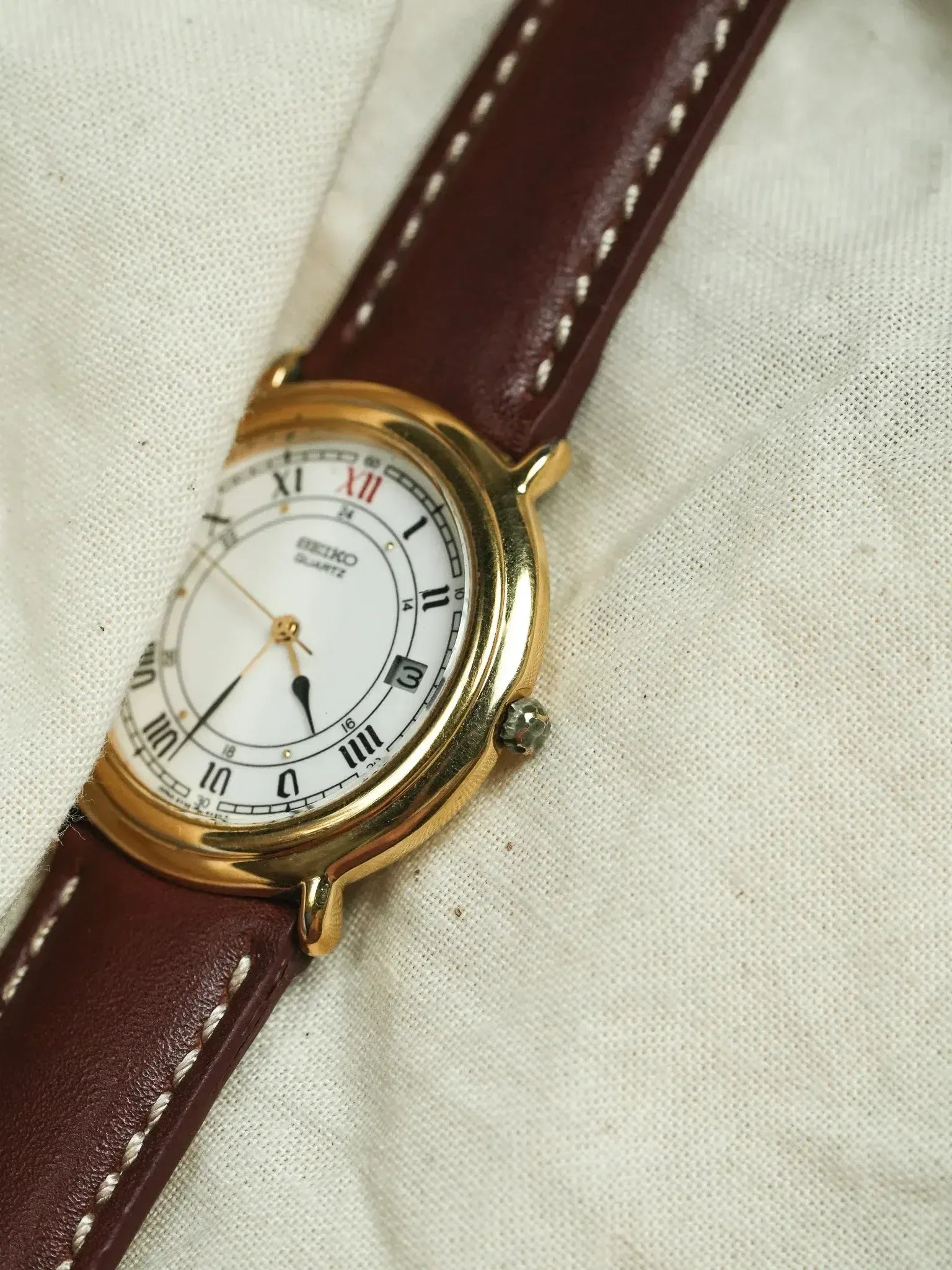 Seiko vintage watch with gold case, white dial, Roman numerals, and brown leather strap