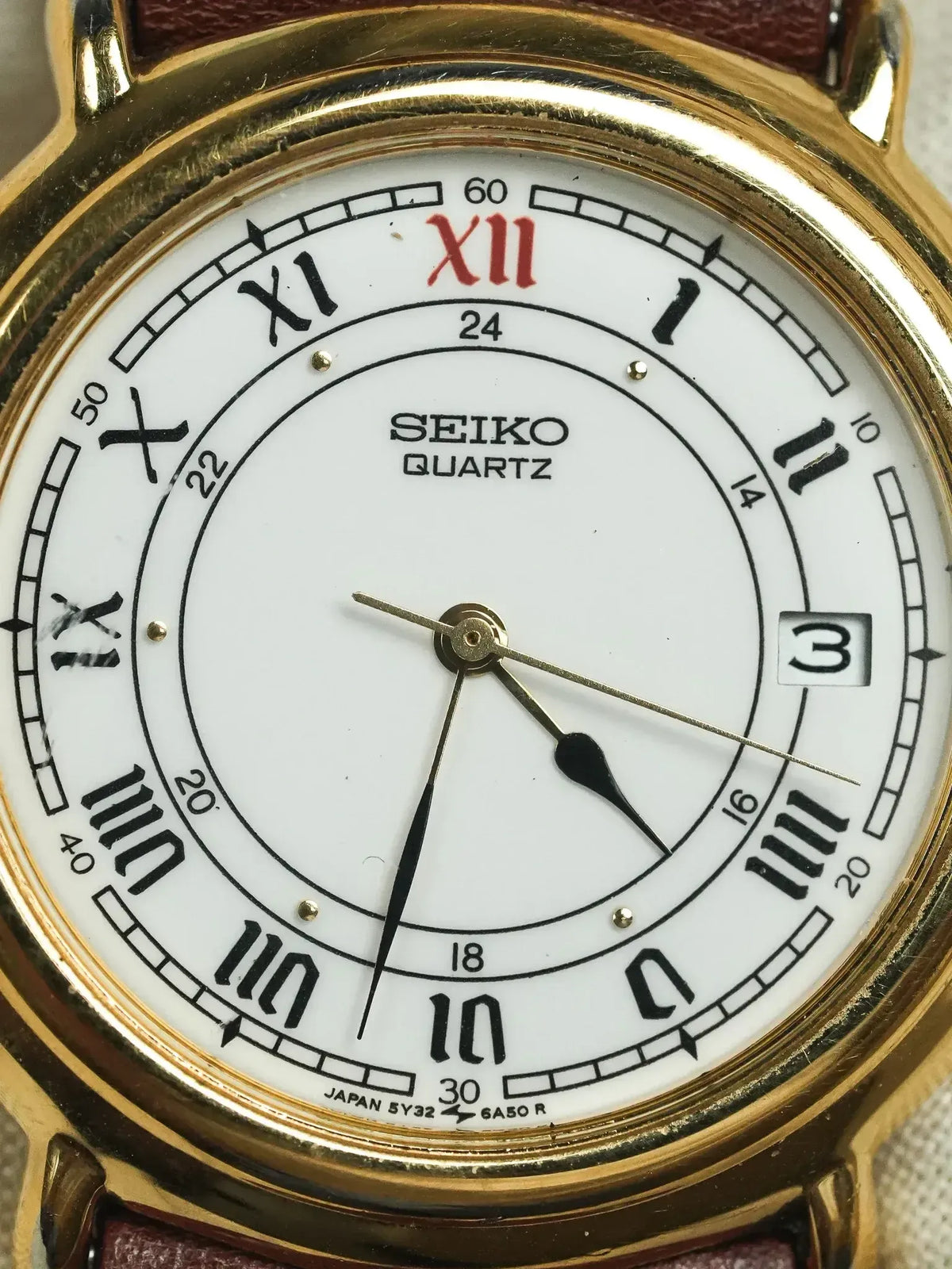 Seiko Quartz vintage watch with gold case, white dial, Roman numerals, and brown leather strap