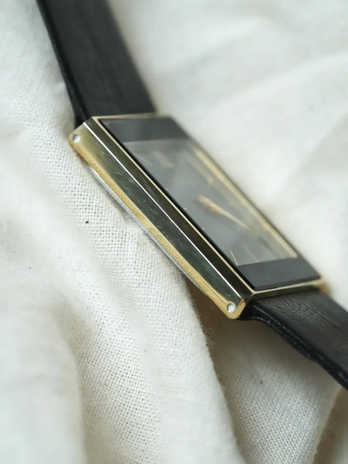 Vintage Cartier watch with gold case, black dial, and black leather strap on white fabric