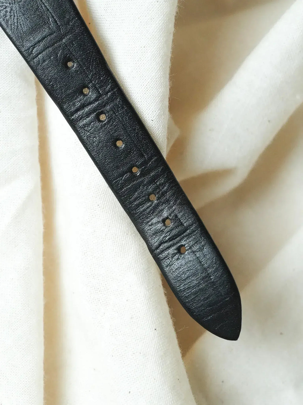Black leather watch strap with visible stitching and adjustment holes on white fabric