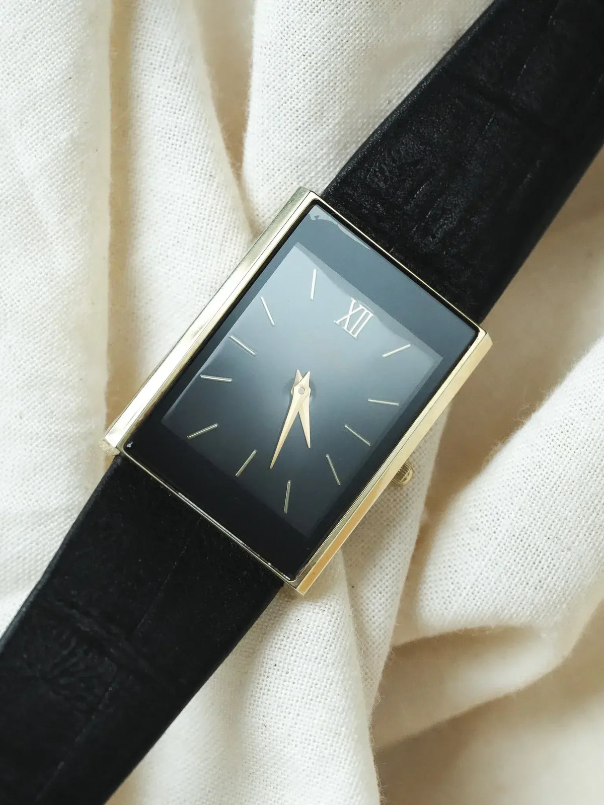 Vintage rectangular watch with black dial, gold case, Roman numeral XII, black leather strap