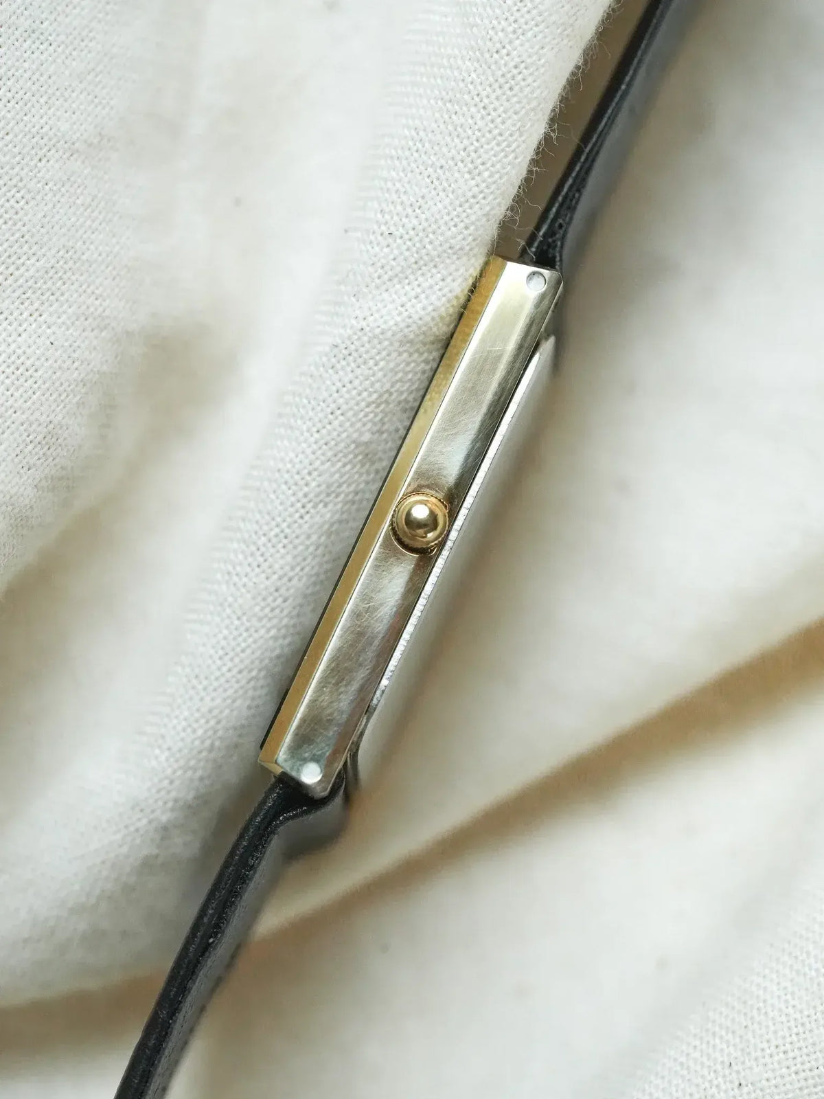 Cartier Tank vintage watch with gold accents and black leather strap on white fabric