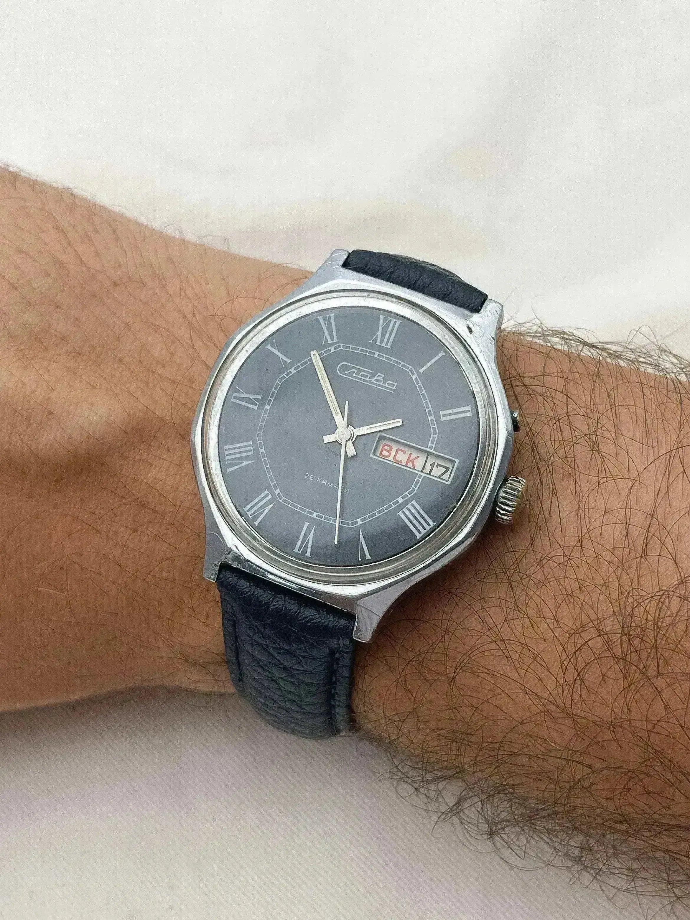 Vintage Slava watch with grey dial, Roman numerals, black leather strap worn on wrist