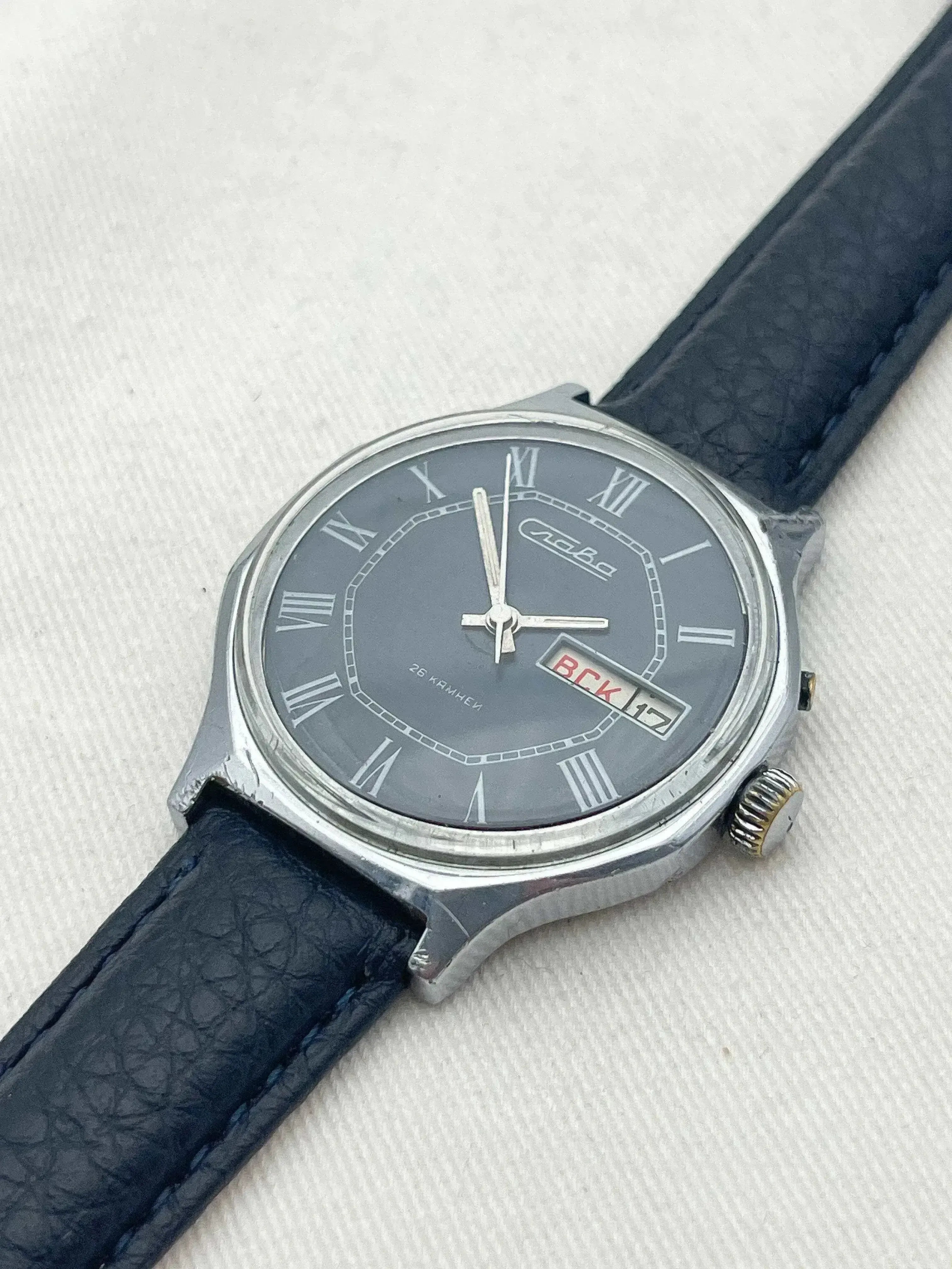 Slava vintage watch with grey dial, Roman numerals, black leather strap on textured background