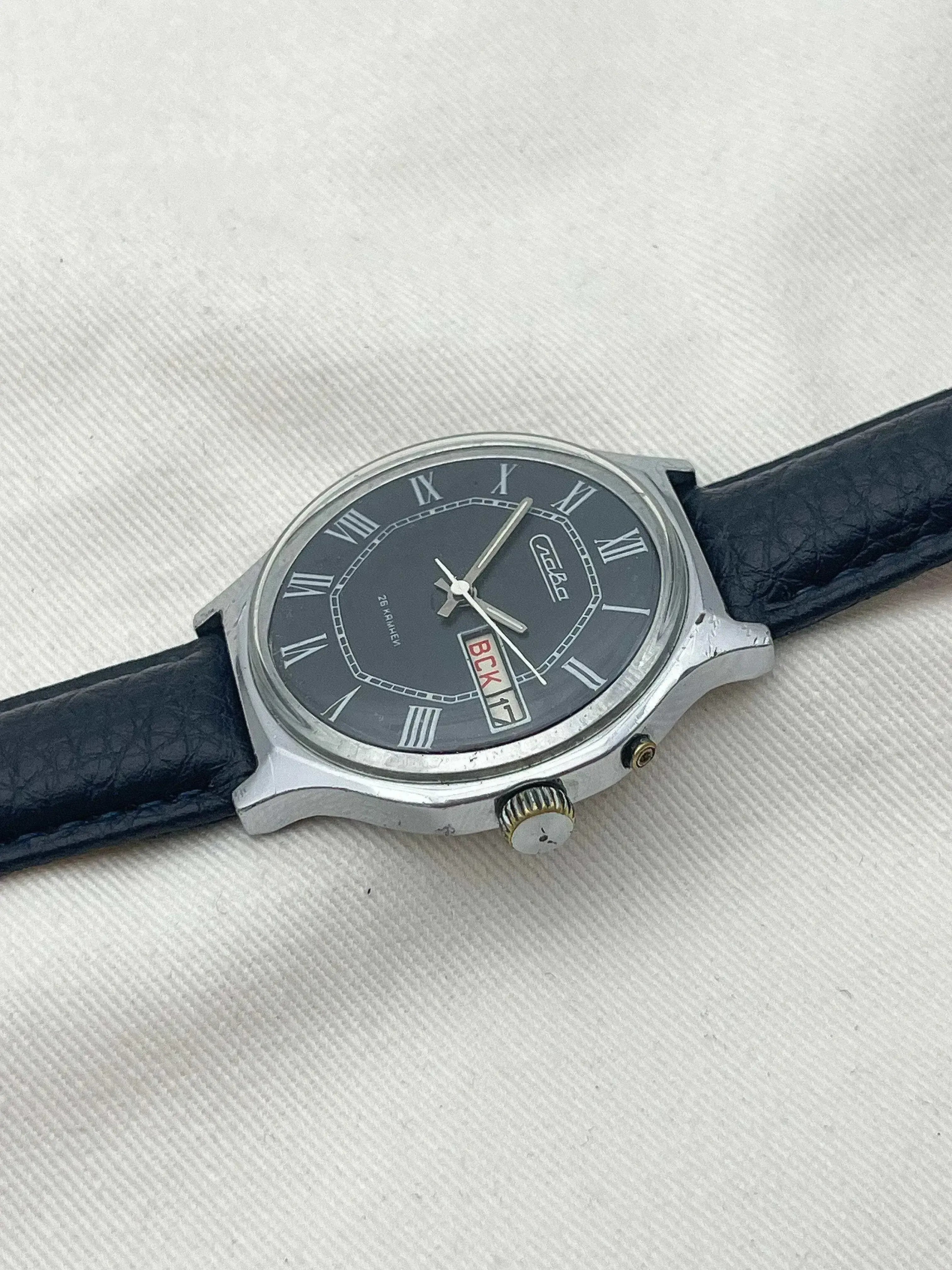 Vintage Vostok watch with black dial, Roman numerals, and black leather strap on textured white background