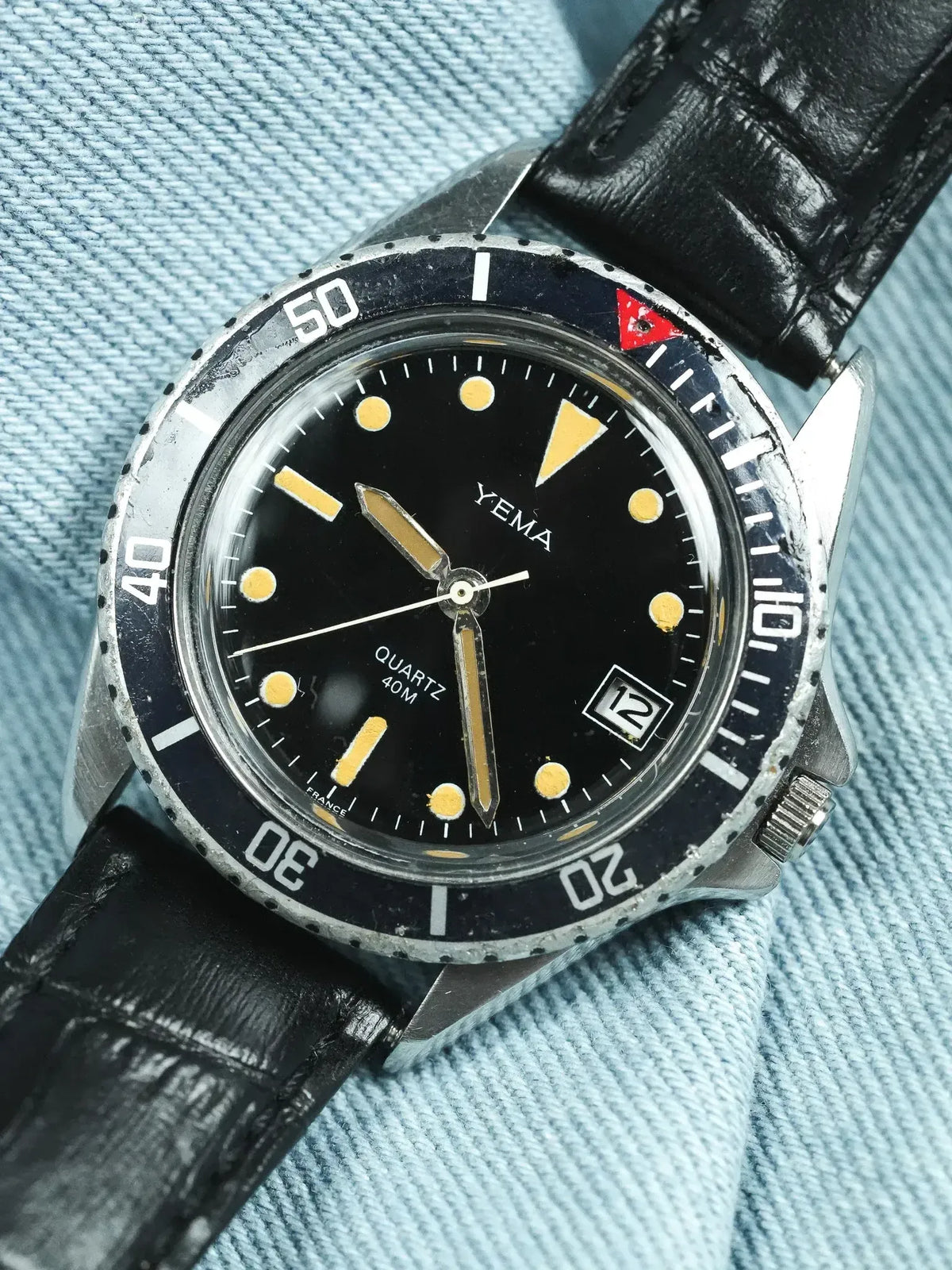 Vintage Yema diver watch with black dial, luminous markers, and black leather strap on denim