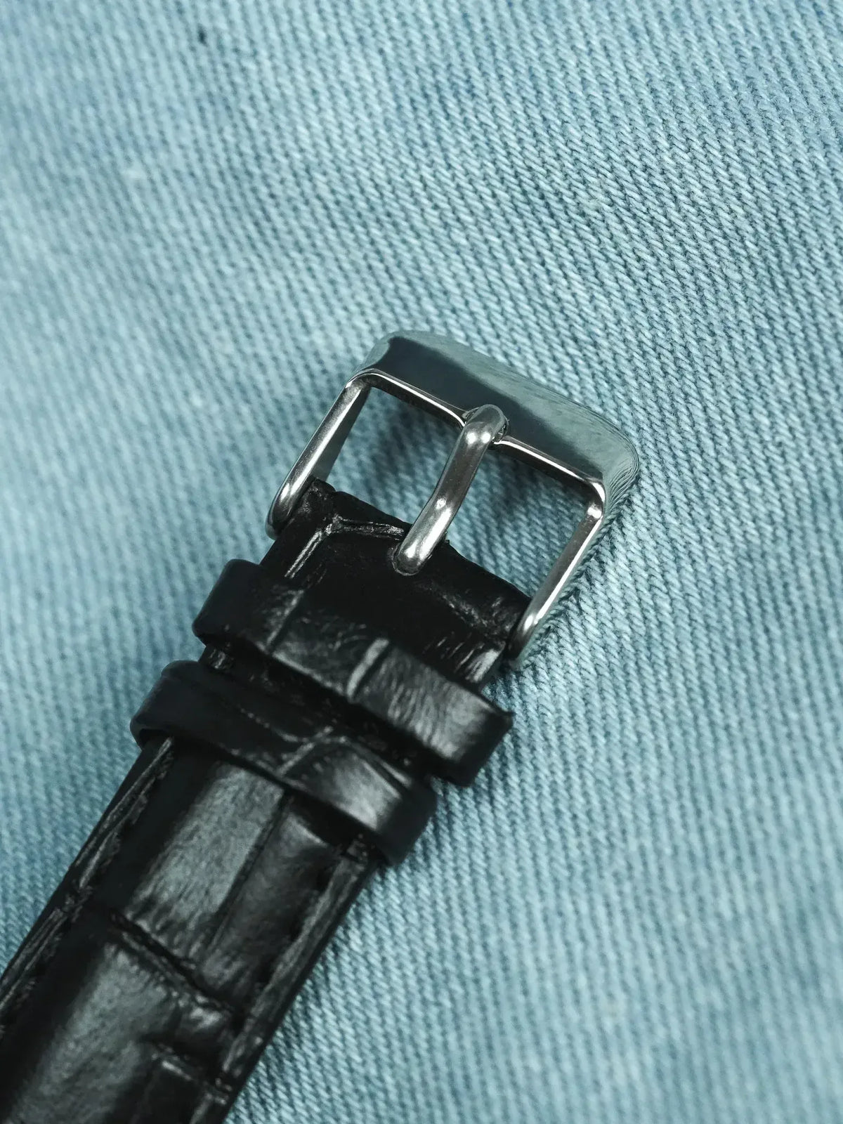 Black alligator leather watch strap with polished steel buckle on denim