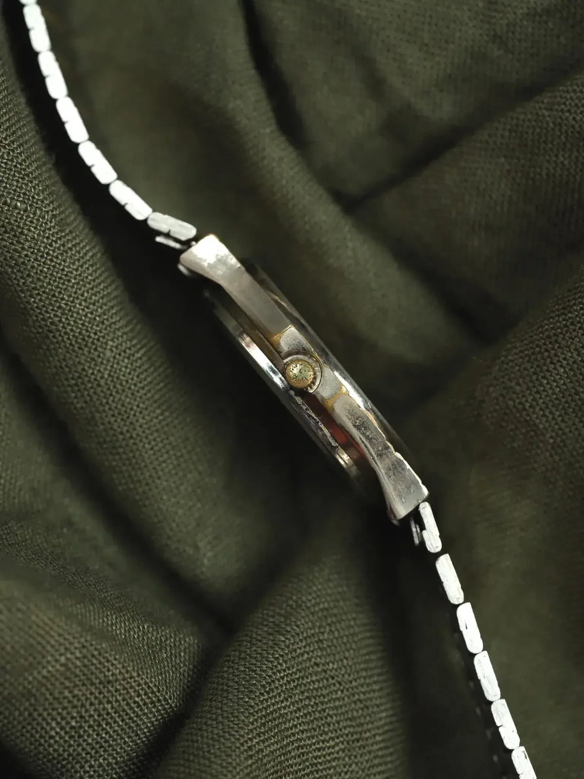 Vintage Omega watch side view, steel case, textured bracelet on dark fabric