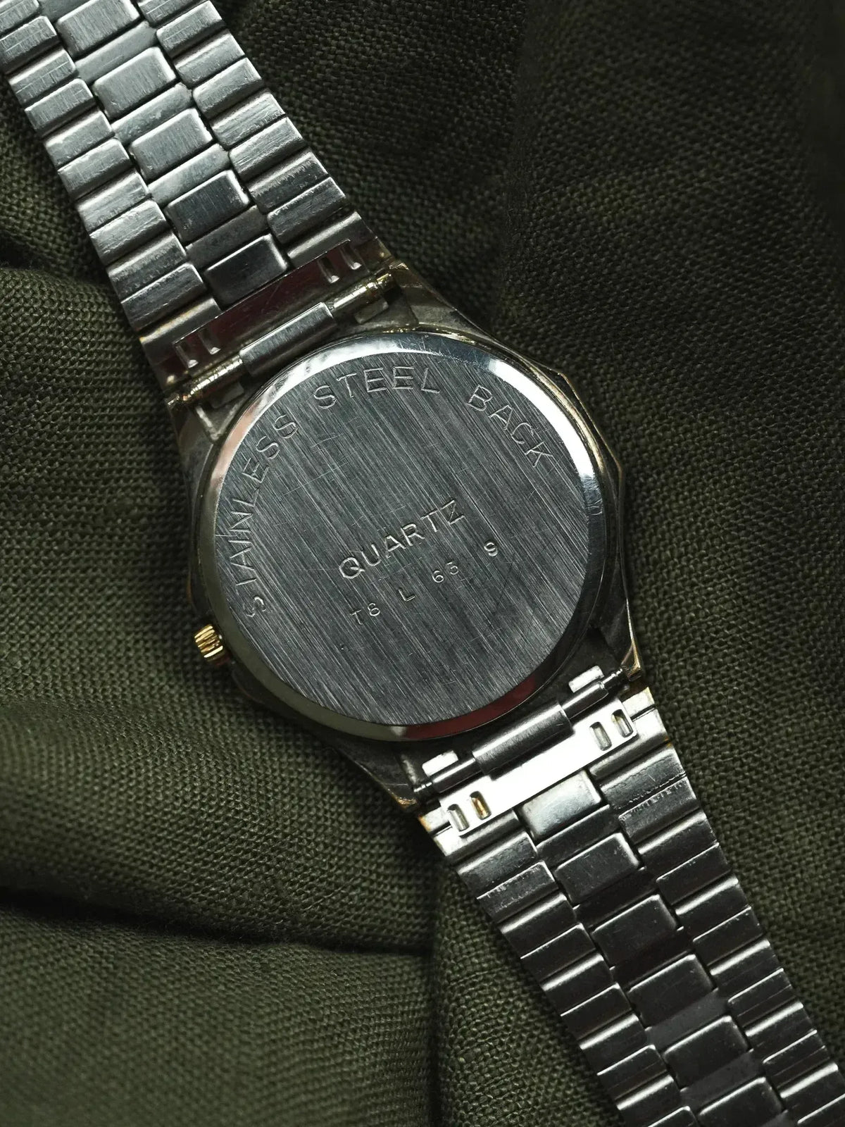 Vintage quartz watch with stainless steel back and bracelet, resting on green fabric