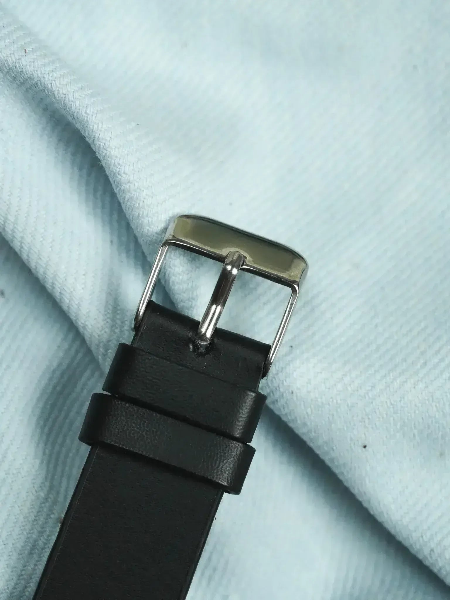 Black leather watch strap with polished steel buckle on light fabric
