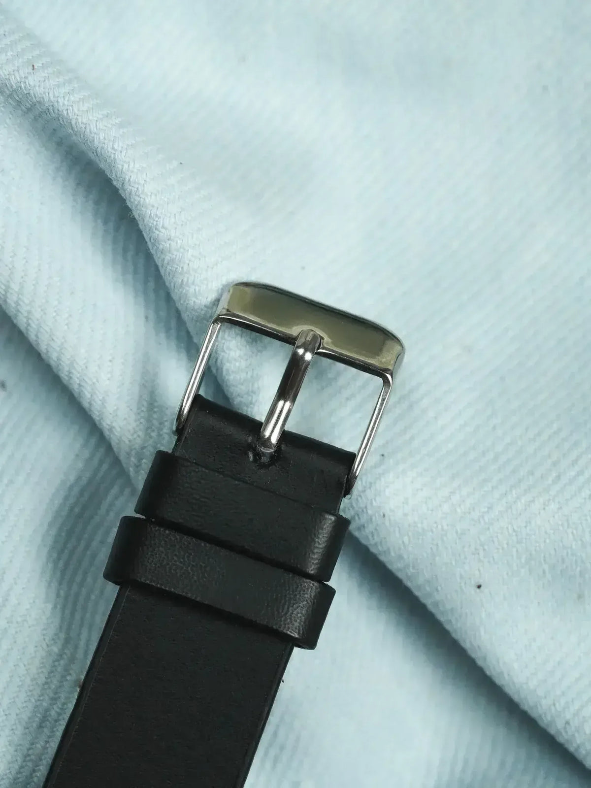 Black leather watch strap with polished steel buckle on light fabric