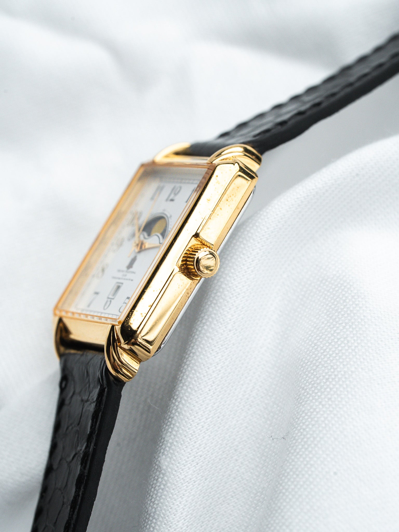 Cartier Tank vintage watch with gold case, white dial, black leather strap on white fabric