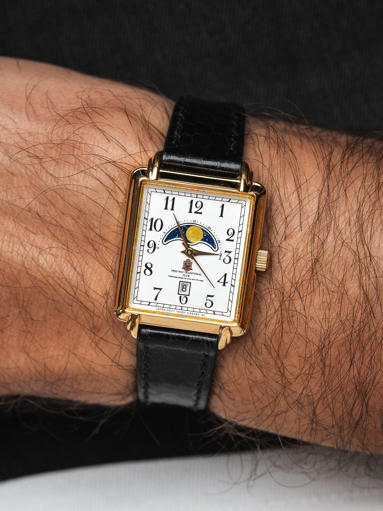 Vintage rectangular gold watch with moon phase, white dial, black leather strap on wrist